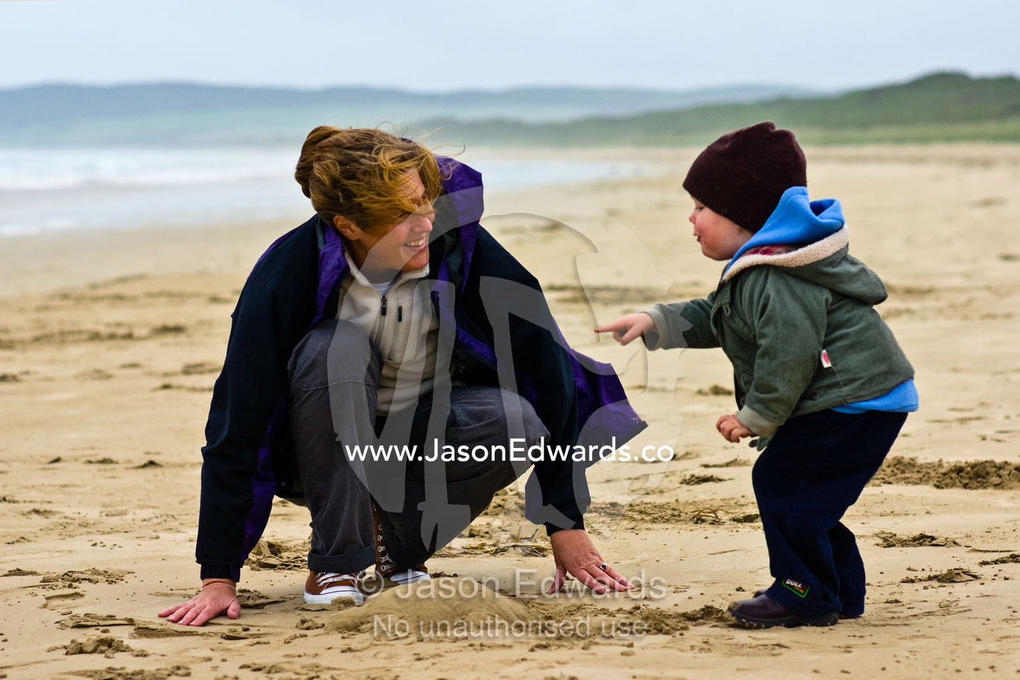 A mother and son build a sand castle on a stormy beach in winter. Sandy Point, Victoria, Australia