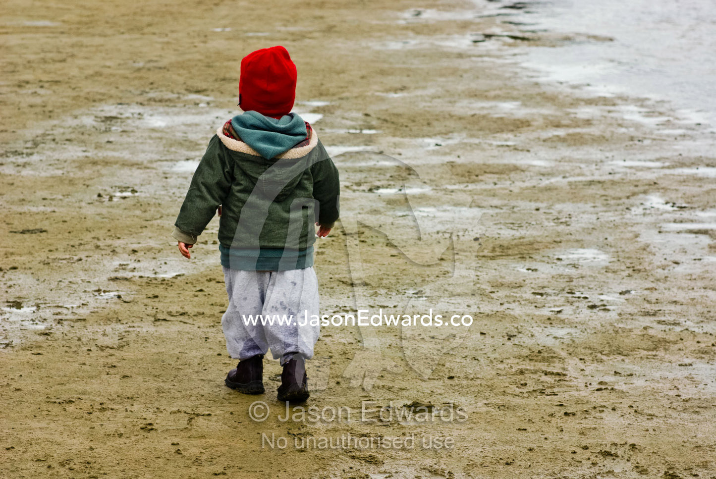 A small boy dressed in winter clothes walking along a river shore. Tidal River, Wilsons Promontory National Park, Victoria, Australia