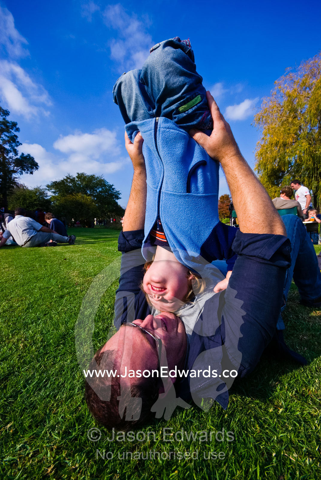 A father and his small son wrestling on a green, manicured lawn. Langwarrin, Victoria, Australia