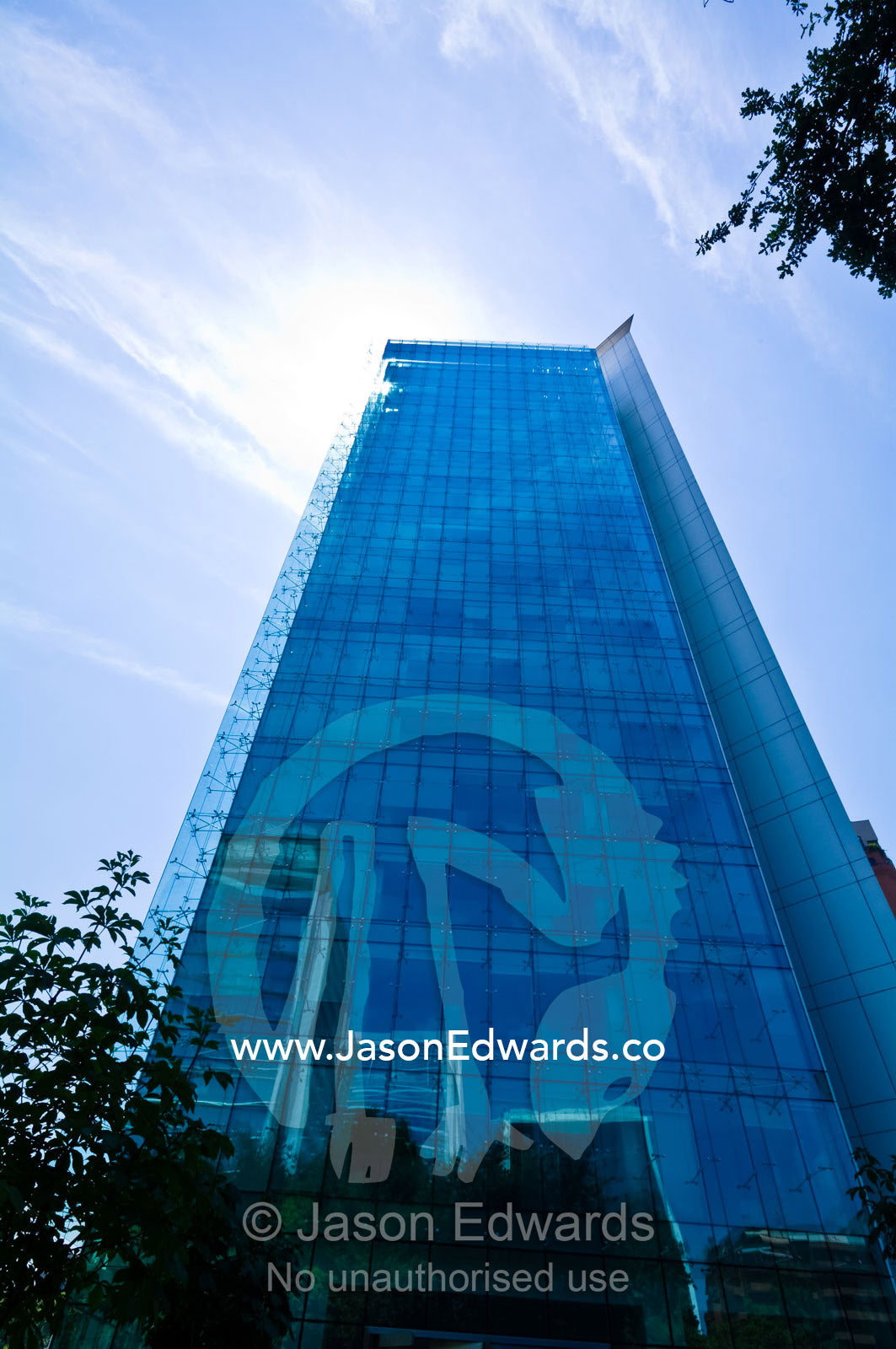 A modern glass office tower rises above trees reflecting the blue sky. Providencia, Santiago, Chile