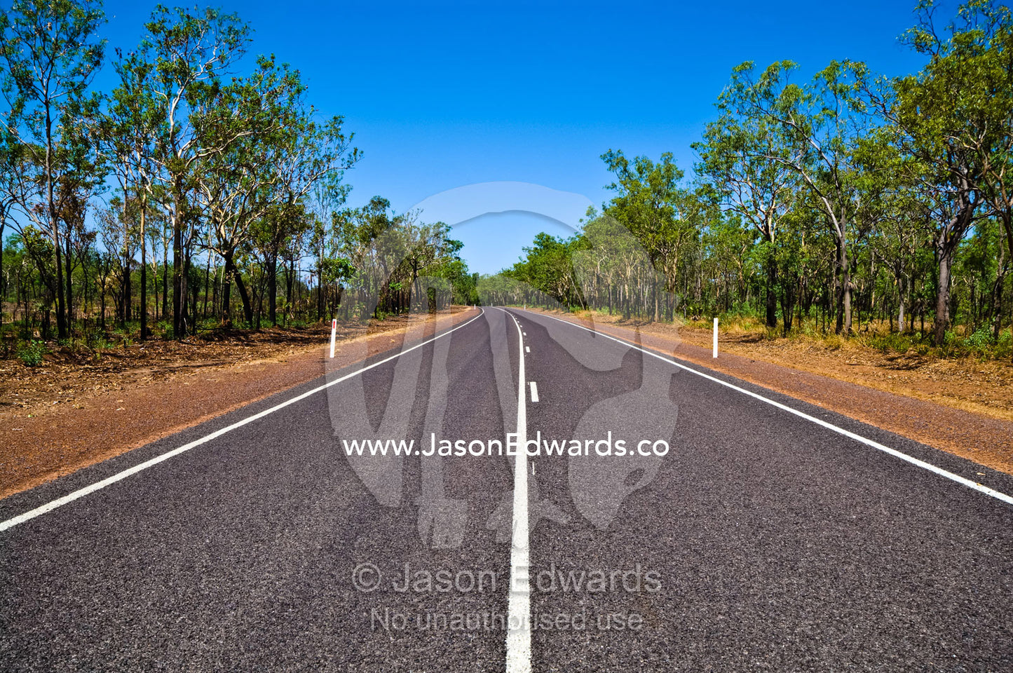 White lines run down the middle of a well-kept road in open woodland. Kakadu Highway, Northern Territory, Australia