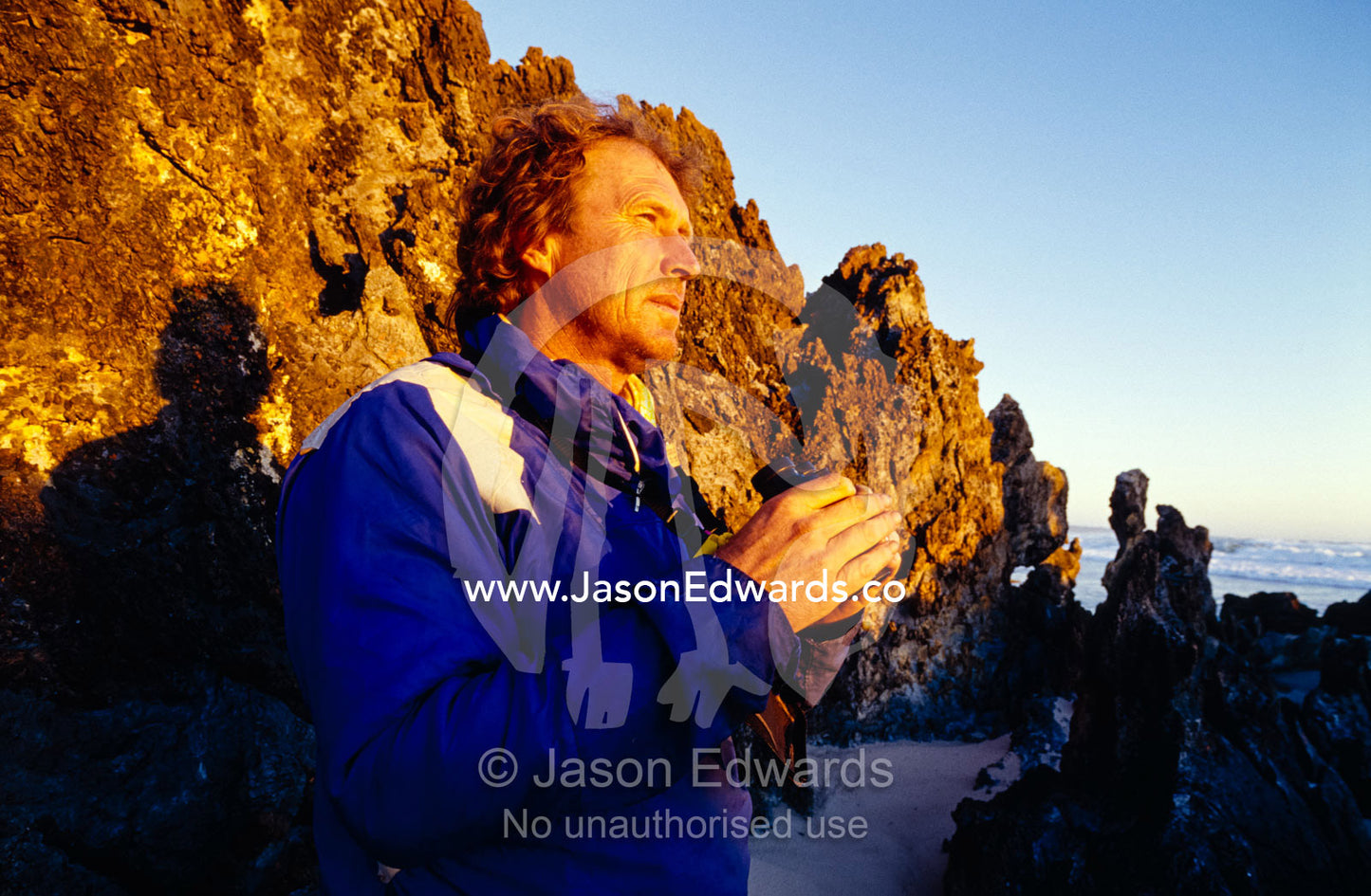A Tasmanian Devil researcher scans a rugged coastline with binoculars. South West Conservation Area, Tasmania, Australia