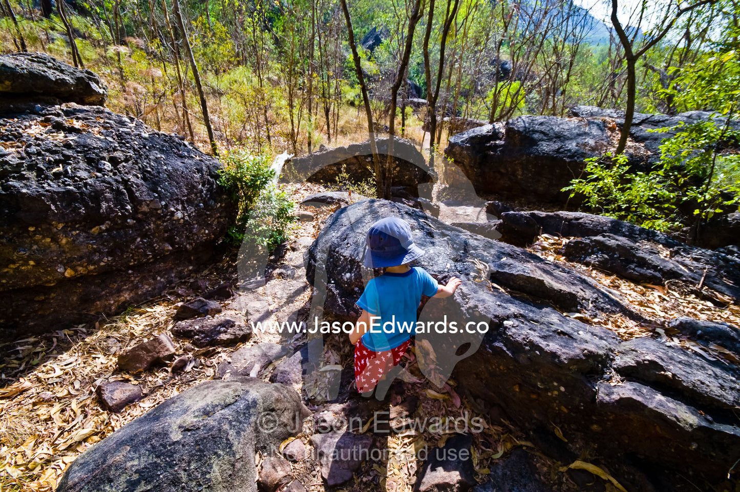 A small boy clambers over rocky terrain whilst exploring the wilds. Kakadu National Park, Northern Territory, Australia.