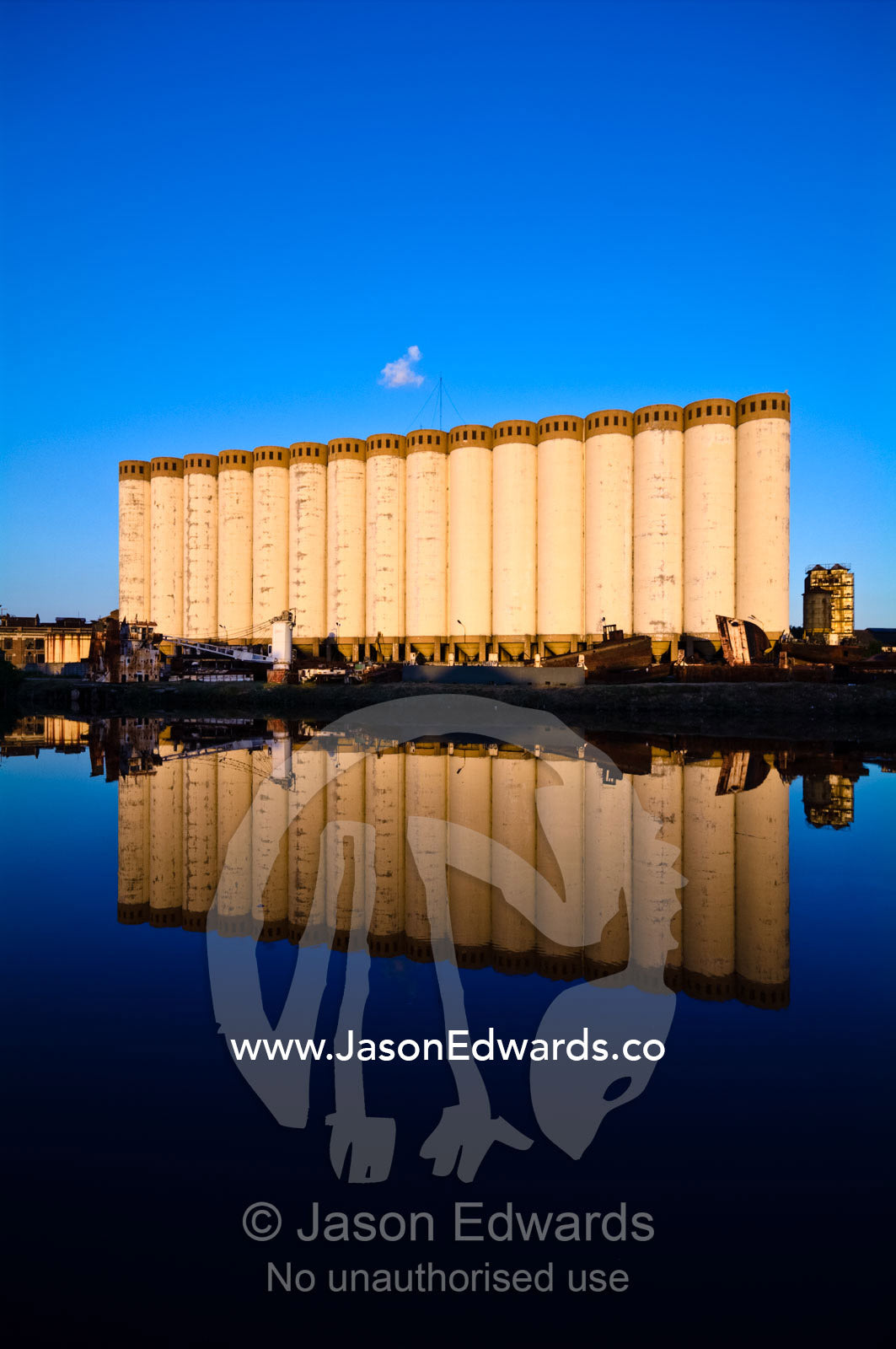 Grain silos and rusting boats reflected in the still waters of a river Riachuelo River, La Boca, Buenos Aires, Argentina.