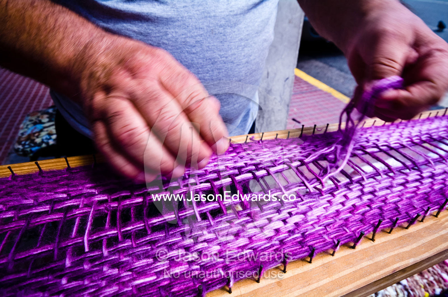 A man weaves an intricate scarf from thick purple wool by hand. Plaza de Mayo, Buenos Aires, Argentina.