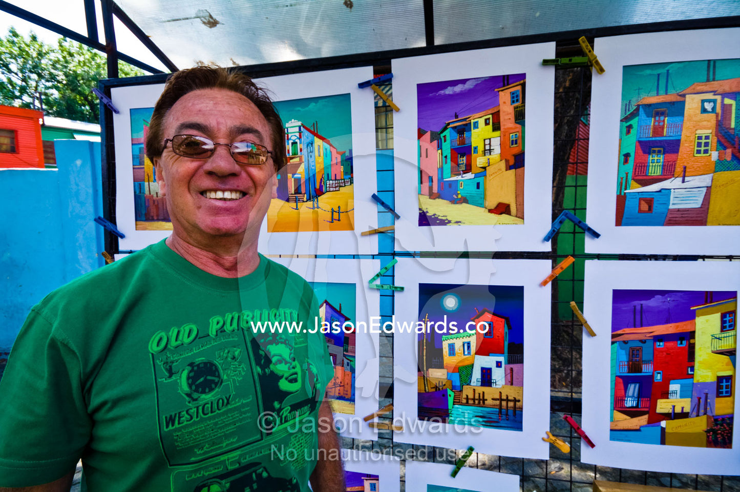 An artist stands proudly by his colorful paintings of La Boca scenes. El Caminito, La Boca, Buenos Aires, Argentina.