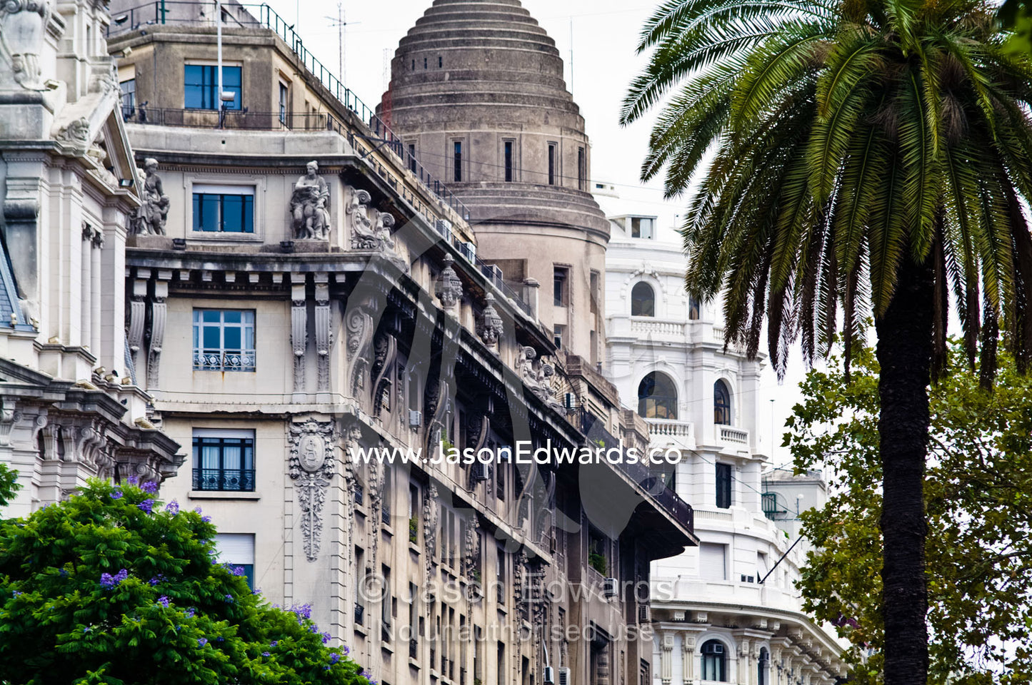 An ornate neo-classical building facade on a palm tree-lined street. Plaza Eva Peron, Avenue Perseo Colon, San Telmo, Buenos Aires, Argentina.