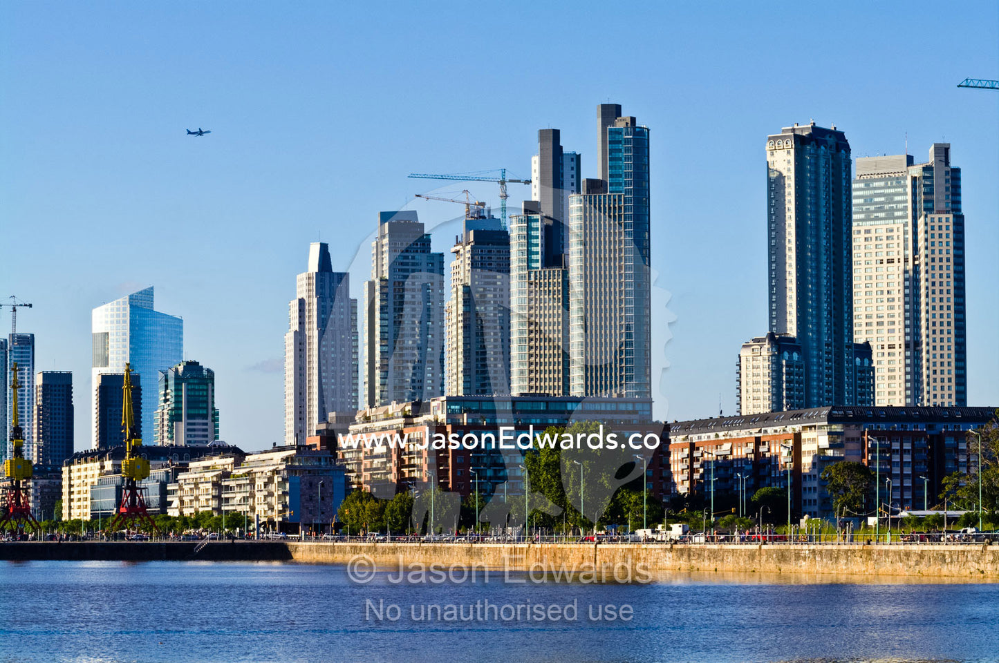A passenger airline flies over a new city skyline under construction. Puerto Madero, Buenos Aires, Argentina.