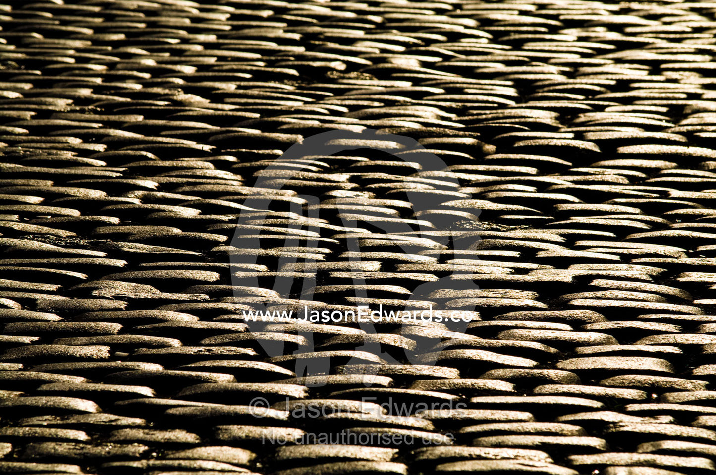 Golden sunlight falls on the textured surface of a cobblestone road. Calle Defensa, San Telmo, Buenos Aires, Argentina.