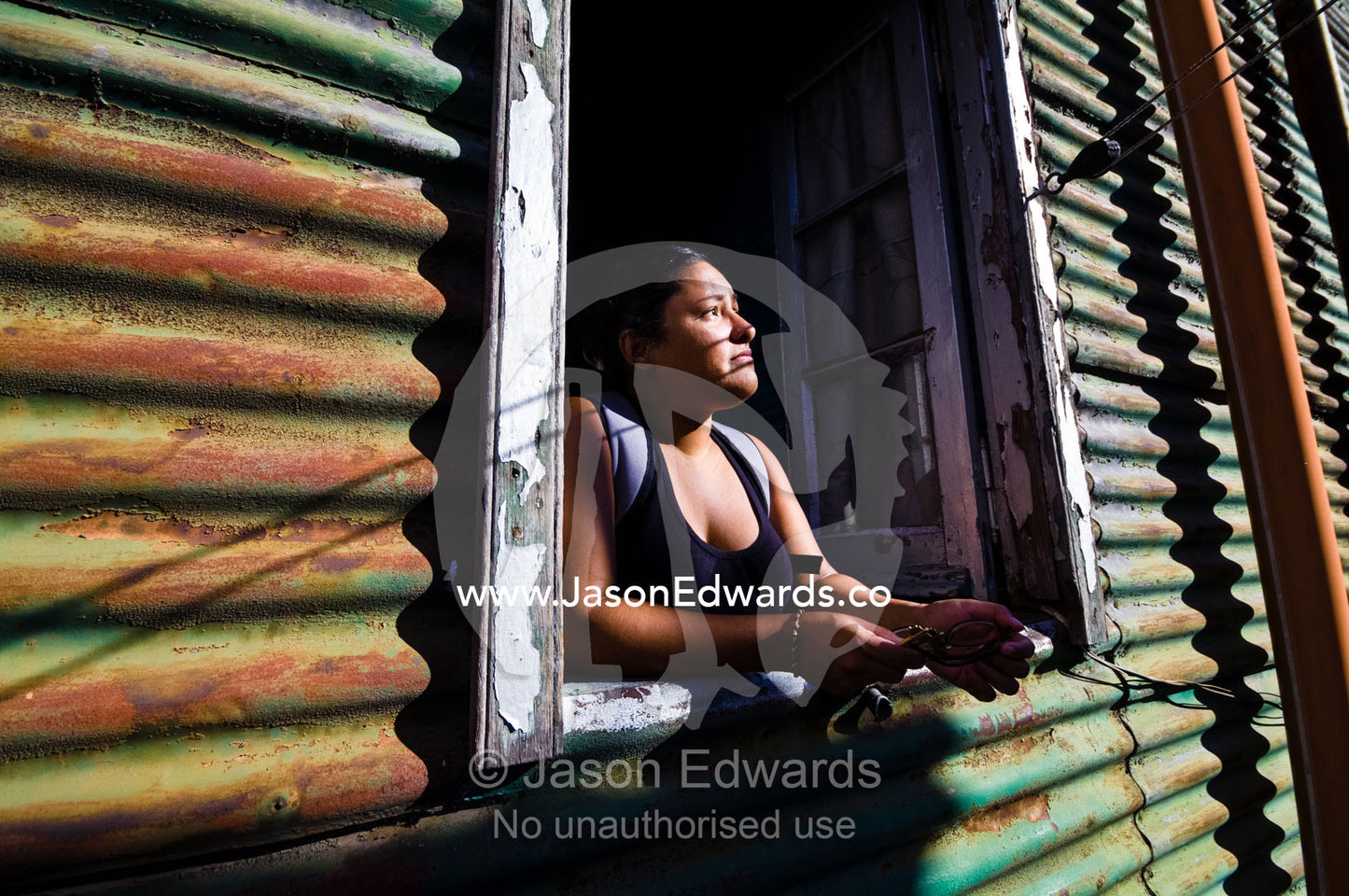 A young woman looks from the window of a corrugated tin conventillo. La Boca, Buenos Aires, Argentina.