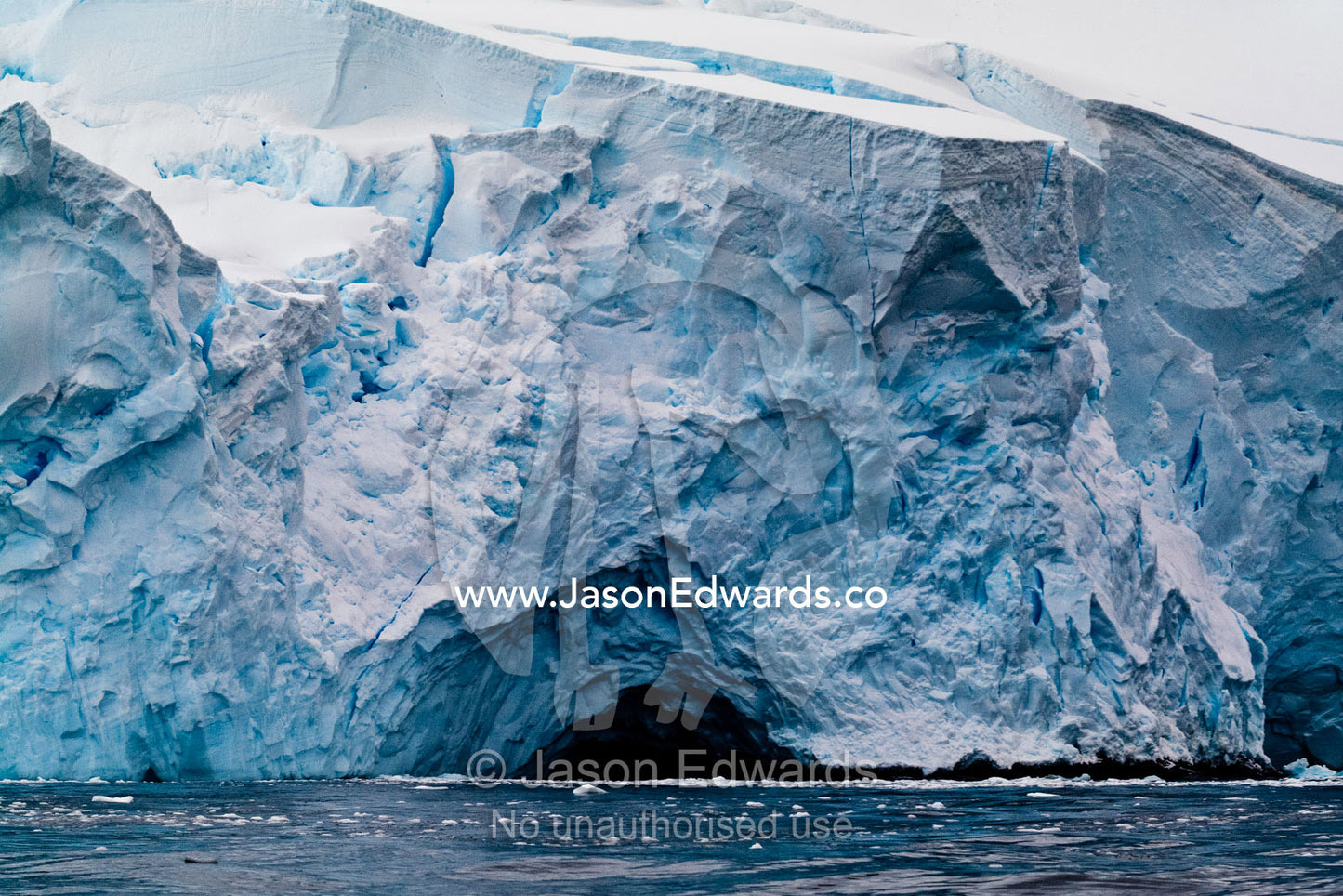 Melting ice water erodes a cave and tunnel in a glacial ice cliff. Crystal Sound, Hanusse Bay, Antarctic Peninsula, Antarctic Circle, Antarctica.
