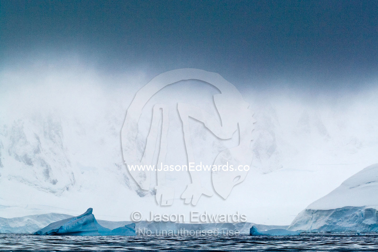 A rugged mountain range rises above the sea into a descending storm. Crystal Sound, Hanusse Bay, Antarctic Peninsula, Antarctic Circle, Antarctica.