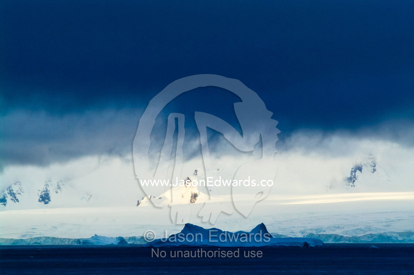 A dense storm descends over a mountain range dwarfing a large iceberg. Crystal Sound, Hanusse Bay, Antarctic Peninsula, Antarctic Circle, Antarctica.