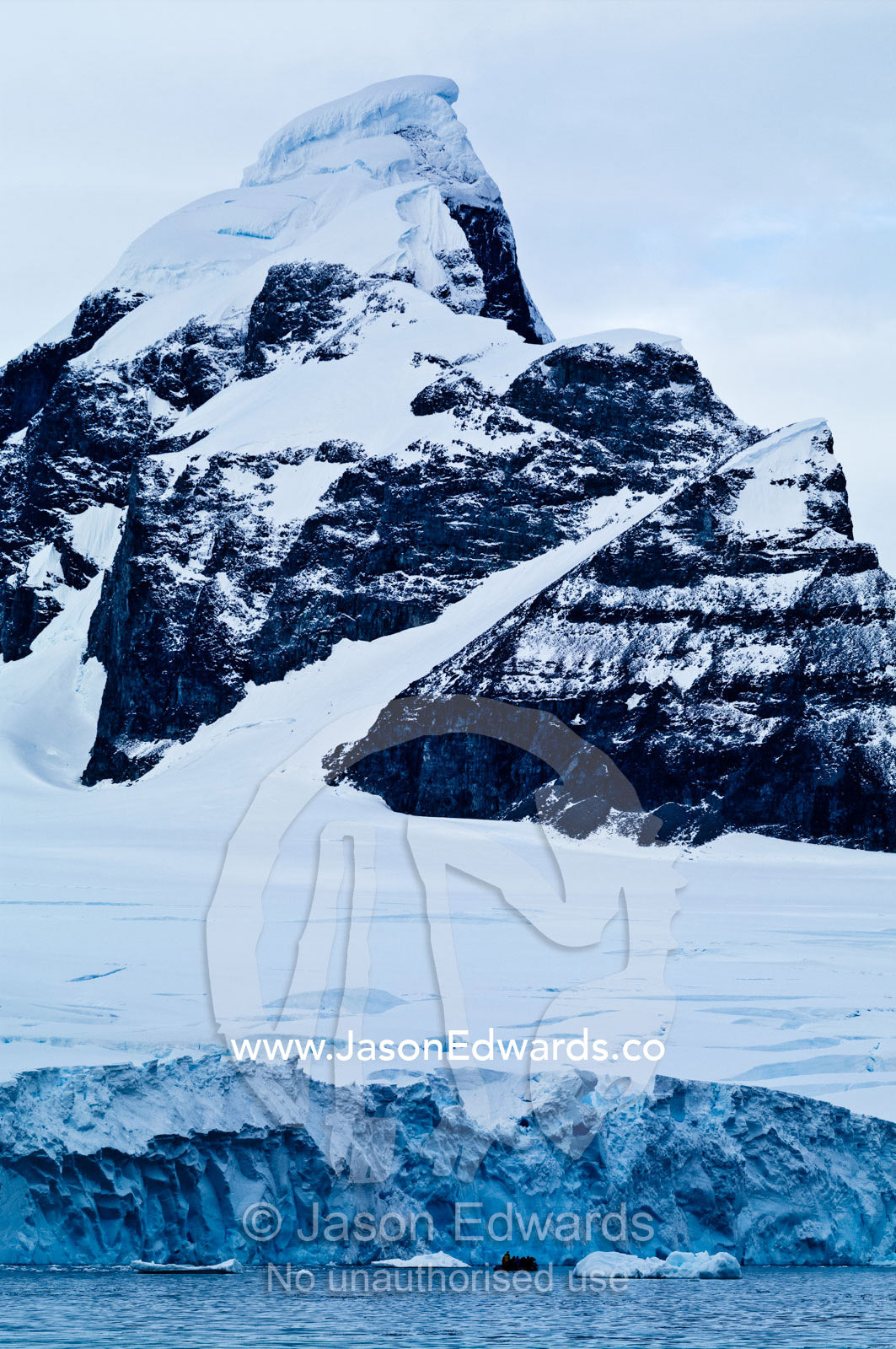 A sheer black mountain summit covered in snow and ice above a glacier. Fish Islands, Flouder Island, The Minnows, Crystal Sound, Antarctic Peninsula, Antarctic Circle, Antarctica.