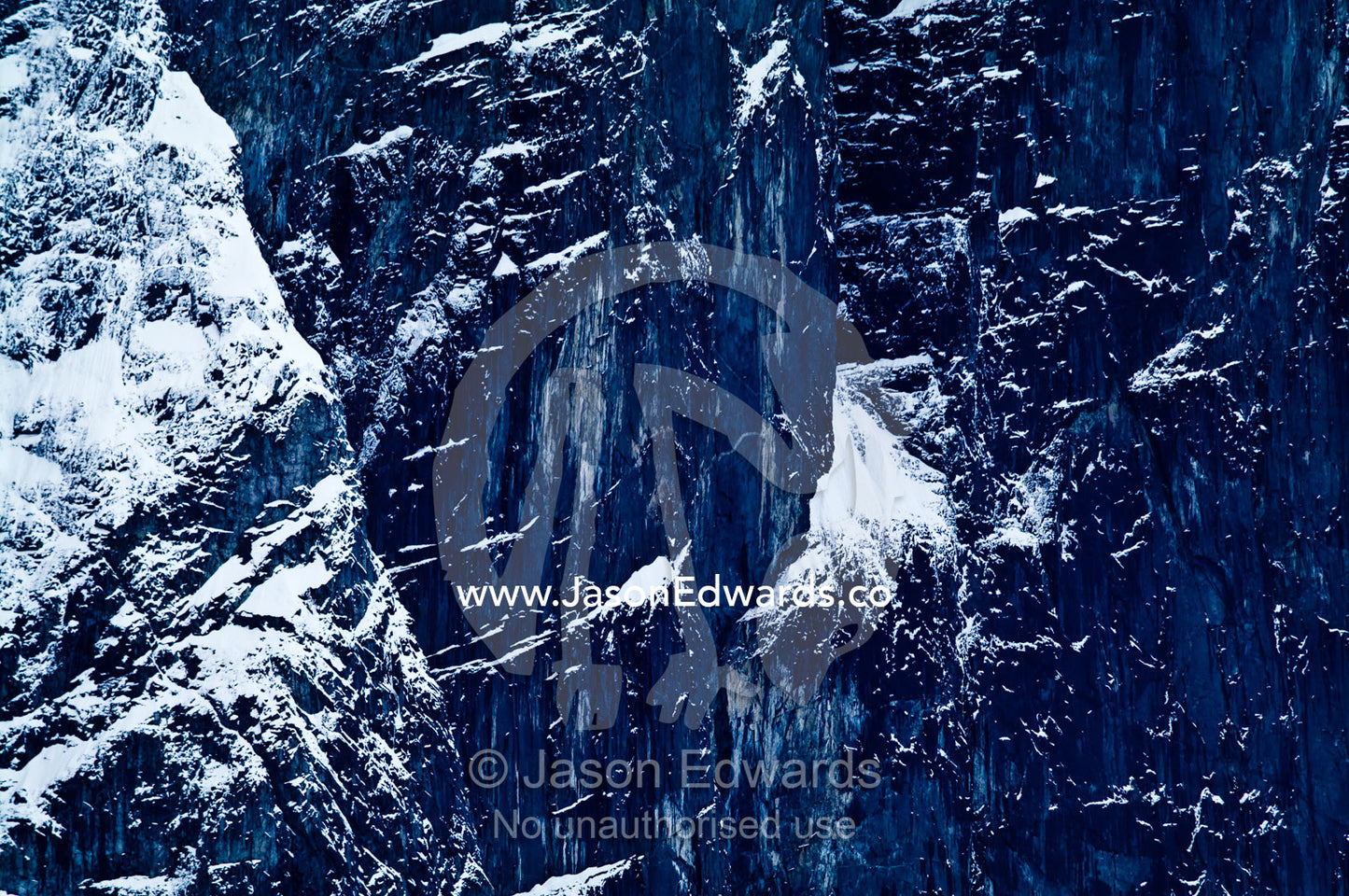 A rugged sheer black mountain cliff face covered in snow and ice. Fish Islands, Flouder Island, The Minnows, Crystal Sound, Antarctic Peninsula, Antarctic Circle, Antarctica.