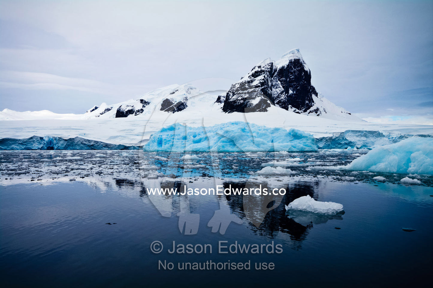 A sheer black mountain summit covered in snow and ice above icebergs. Fish Islands, Flouder Island, The Minnows, Crystal Sound, Antarctic Peninsula, Antarctic Circle, Antarctica.