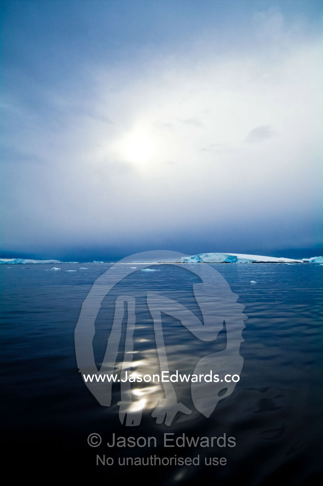 The sun casts ghostly reflected light over the surface of a calm sea. Fish Islands, Flouder Island, The Minnows, Crystal Sound, Antarctic Peninsula, Antarctic Circle, Antarctica.