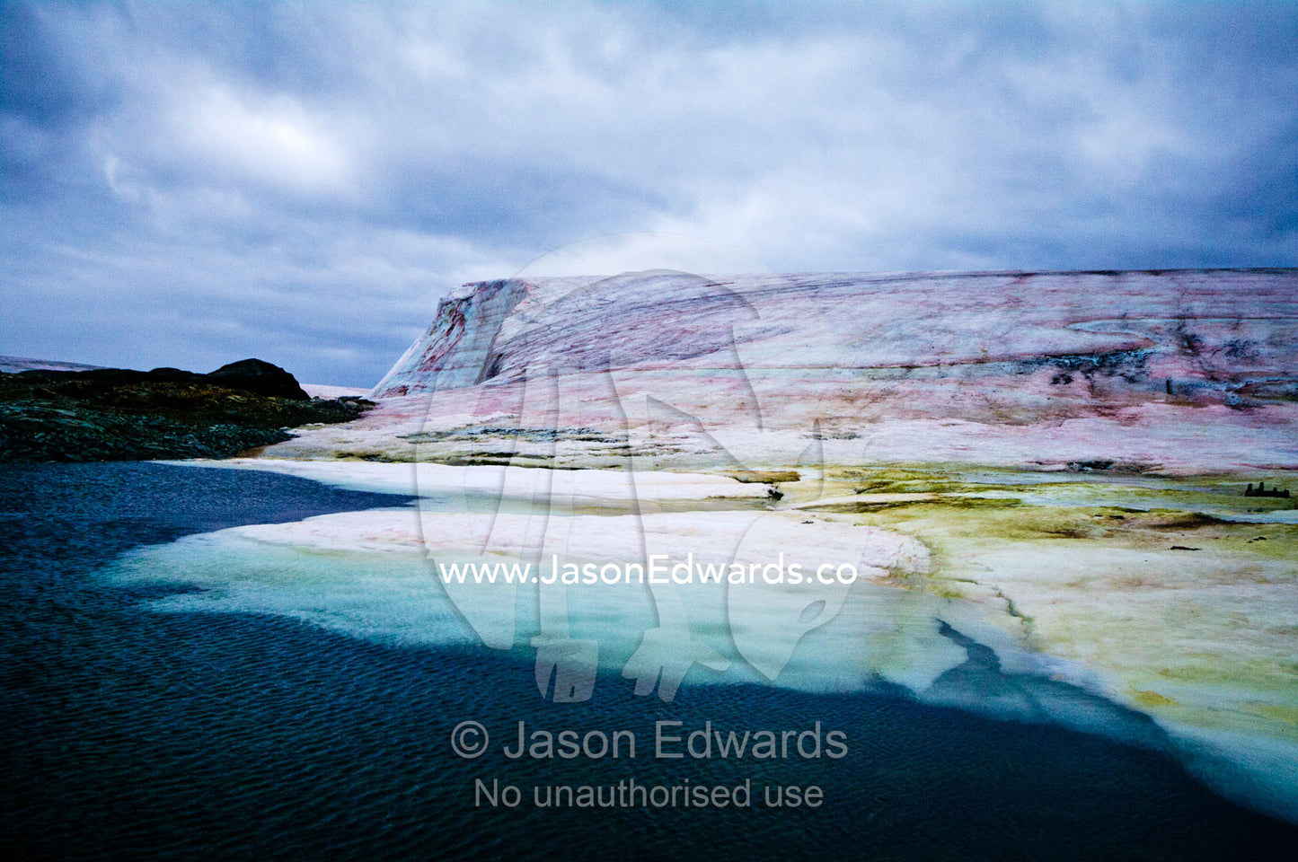 A rugged weathered glacier cap with pink Snow Algae, cryoalgae. Winter Island, Argentine Islands, Faraday Islands, Antarctic Peninsula, Antarctica.