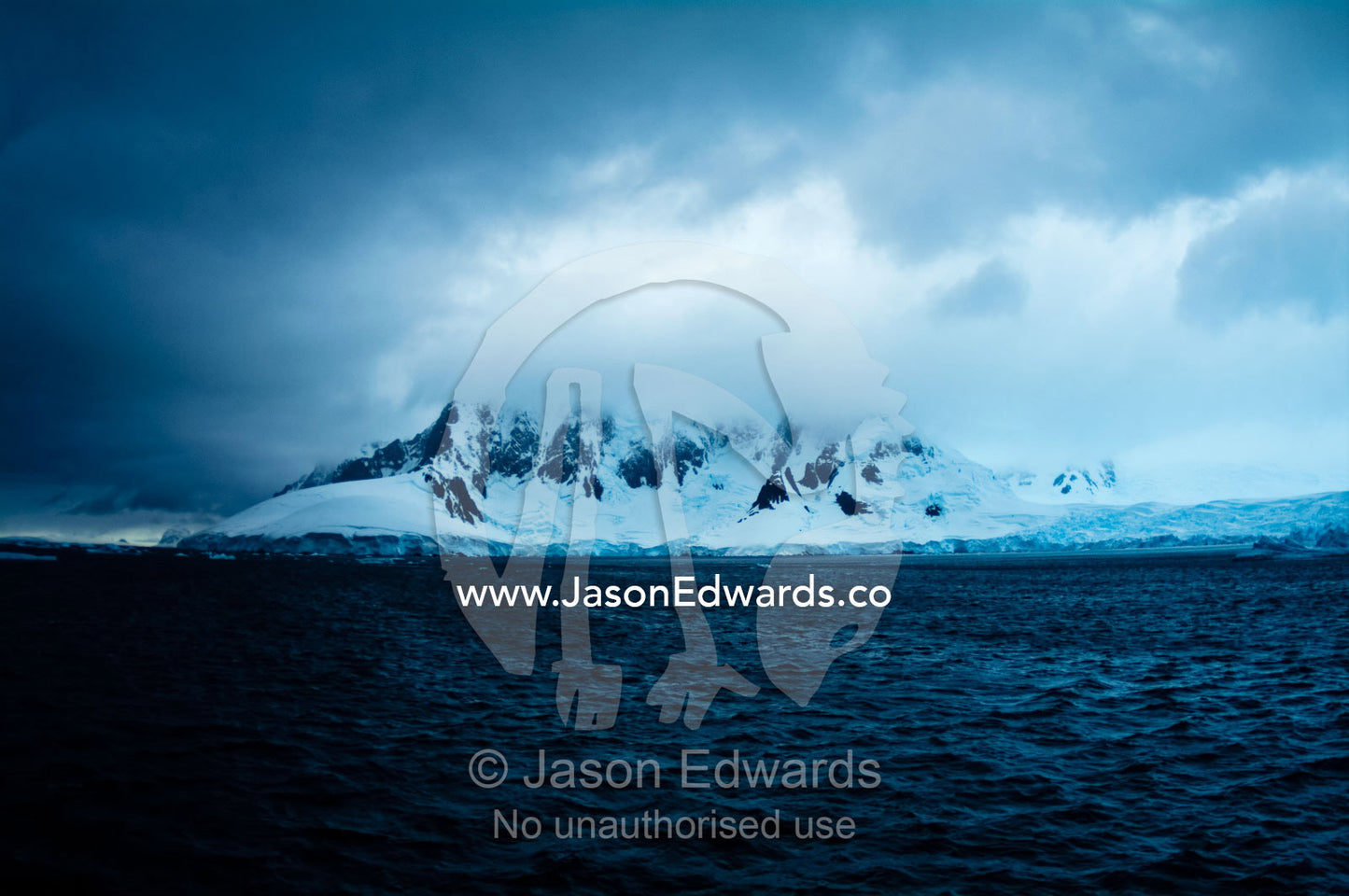 A dark brooding ocean channel between massive stormy mountain peaks. Lemaire Channel, Antarctic Peninsula, Antarctica.