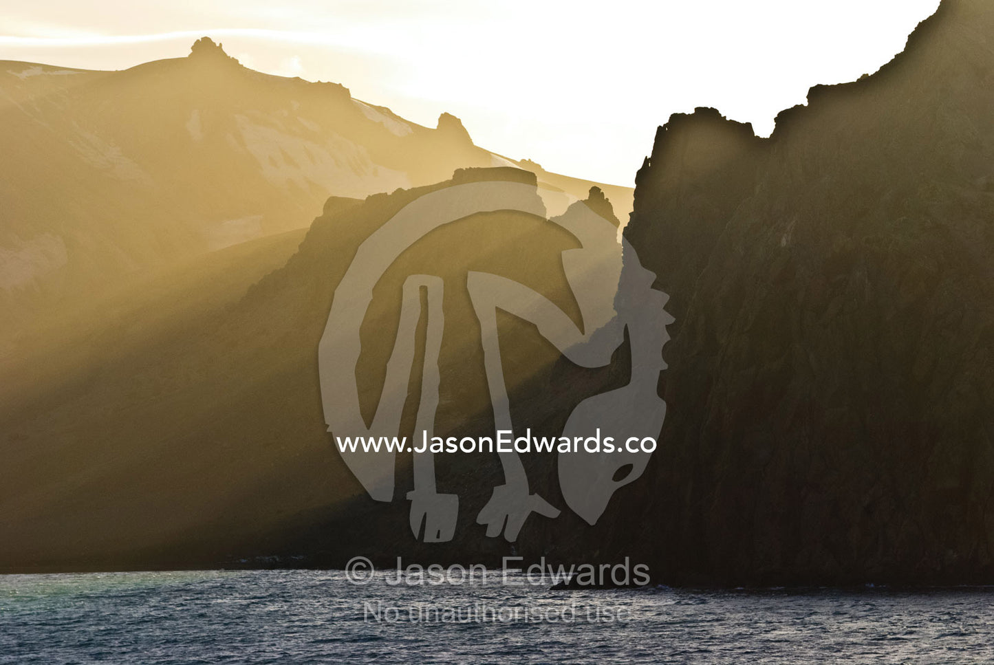 Sunbeams pierce a rugged cliff face surrounding a volcanic caldera. Port Foster, Neptune's Bellows, Deception Island, South Shetland Islands, Antarctic Peninsula, Antarctica.