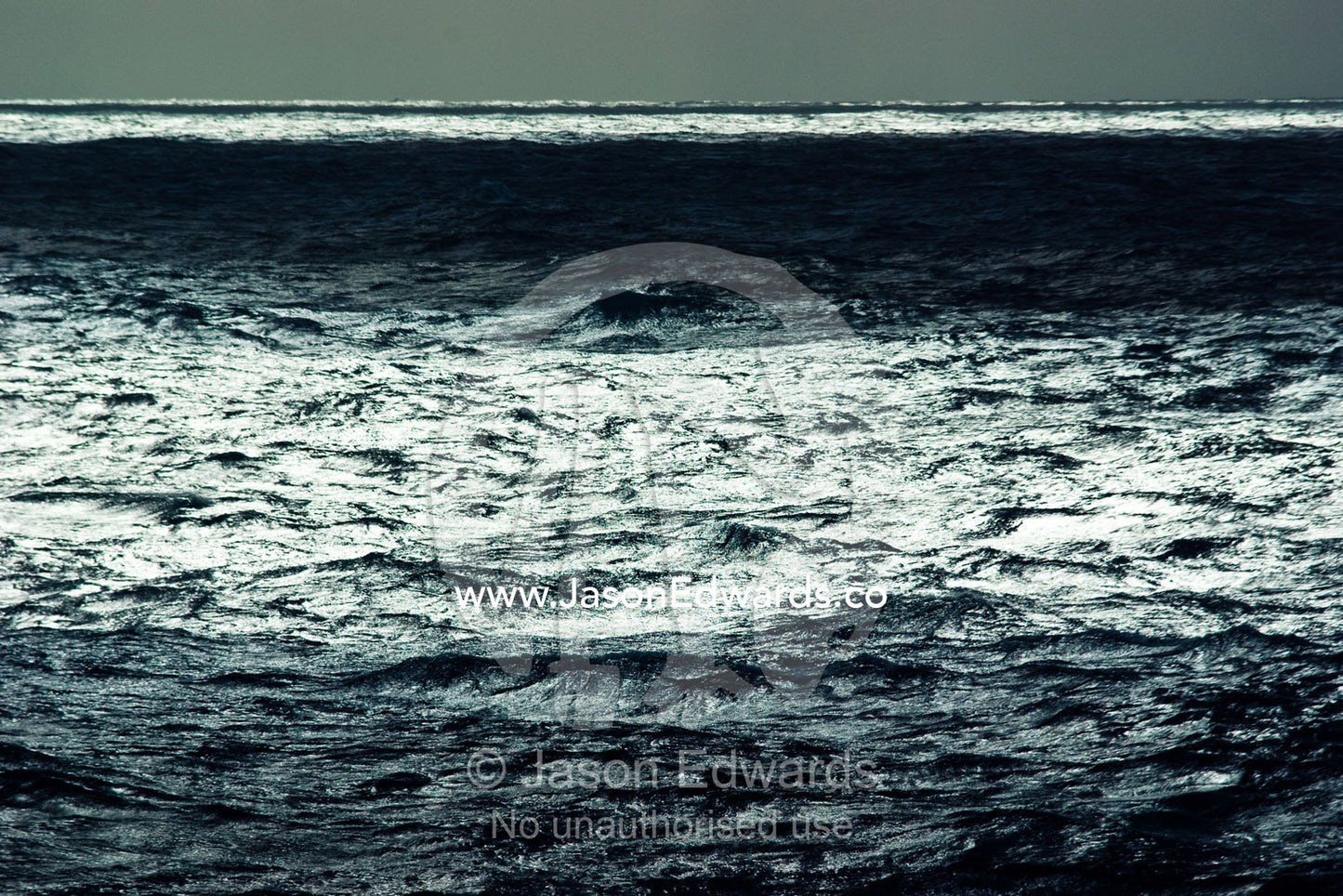 Sunbeams pierce a grey clouds on a stormy featureless ocean horizon. The Drake Passage between the Atlantic Ocean and Pacific Ocean.