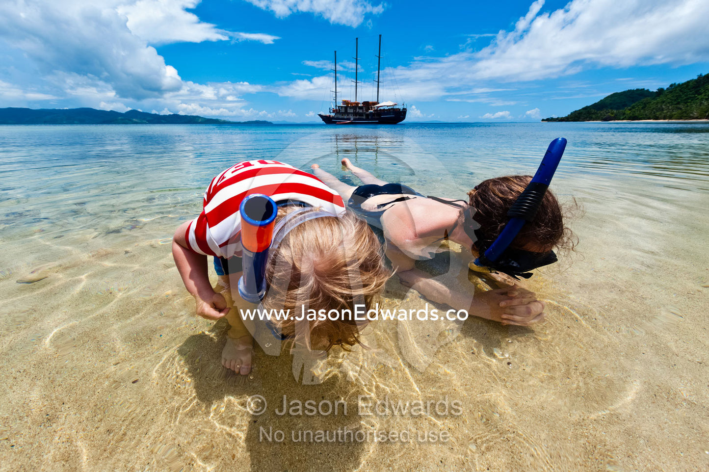 A mother and son search the sand for sea creatures with snorkels. Rabi Island, Somosomo Strait, Pacific Ocean, Fiji Islands.