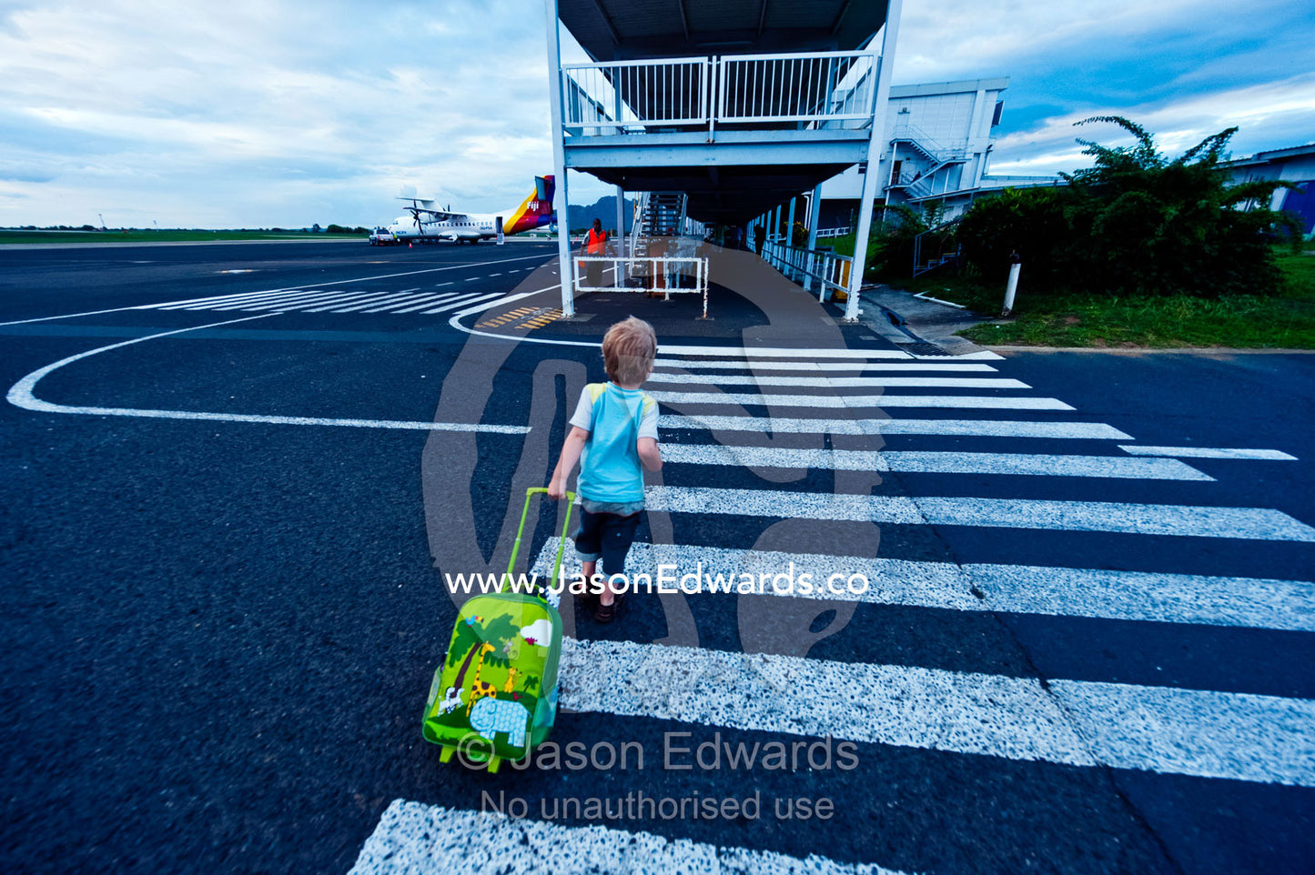 A small boy walks across an airport tarmac with his travel bag. Viti Levu Island, Pacific Ocean, Fiji Islands.