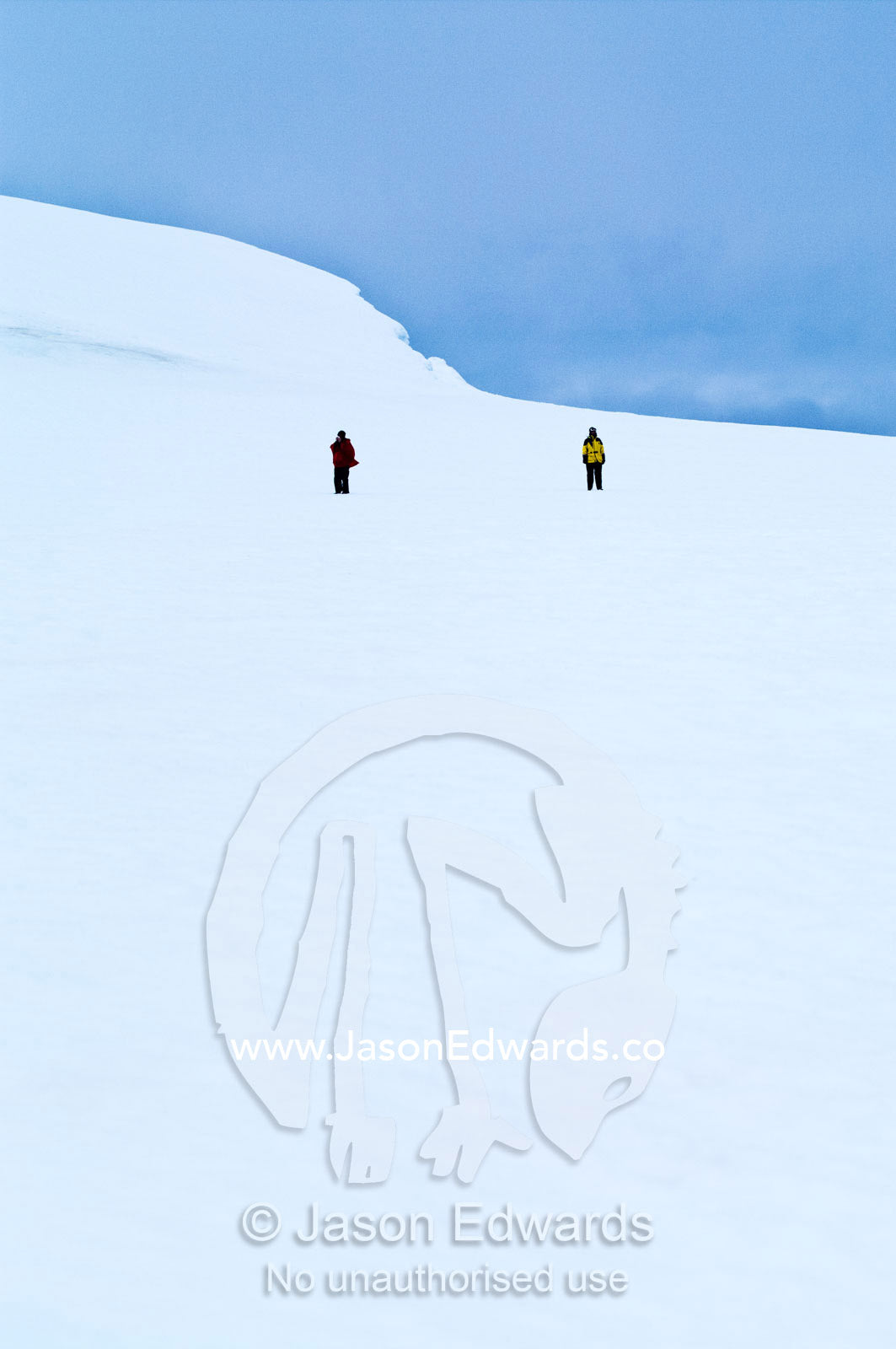 A tourist and guide explore a barren ice slope on a rugged island. Prospect Point, Crystal Sound, Antarctic Peninsula, Antarctic Circle, Antarctica.