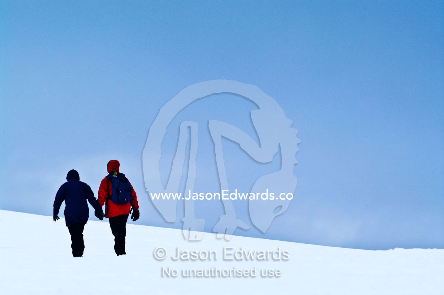 A tourist couple explore a barren ice slope on a rugged island. Prospect Point, Crystal Sound, Antarctic Peninsula, Antarctic Circle, Antarctica.