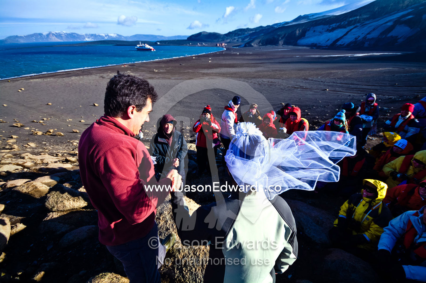 A bride and groom during their wedding ceremony in windy Antarctica. Neptune's Window, Whalers Bay, Antarctic Historic Site, Port Foster, Deception Island, South Shetland Islands, Antarctic Peninsula, Antarctica.