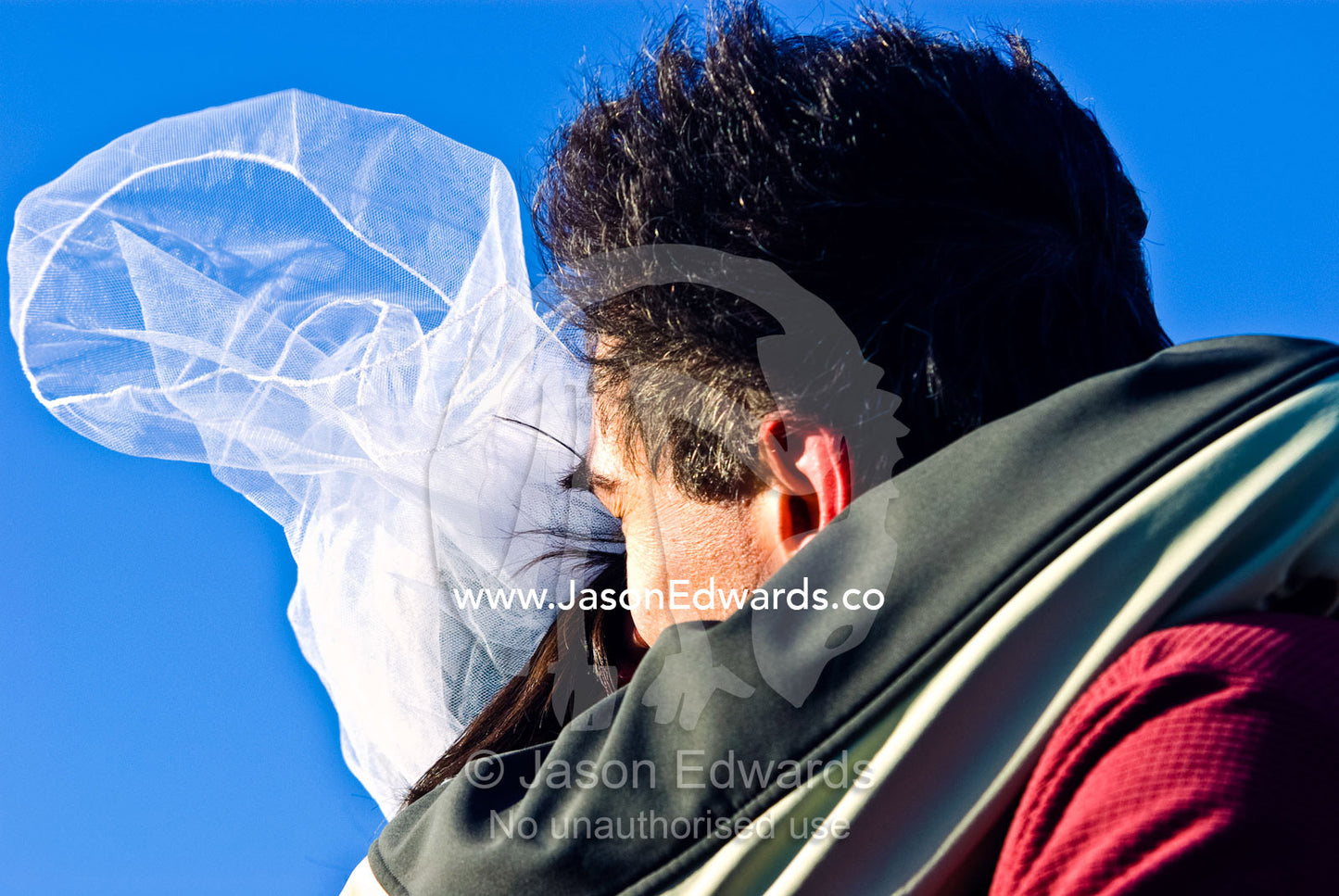 A groom kisses the bride during their windy wedding in Antarctica. Neptune's Window, Whalers Bay, Antarctic Historic Site, Port Foster, Deception Island, South Shetland Islands, Antarctic Peninsula, Antarctica.