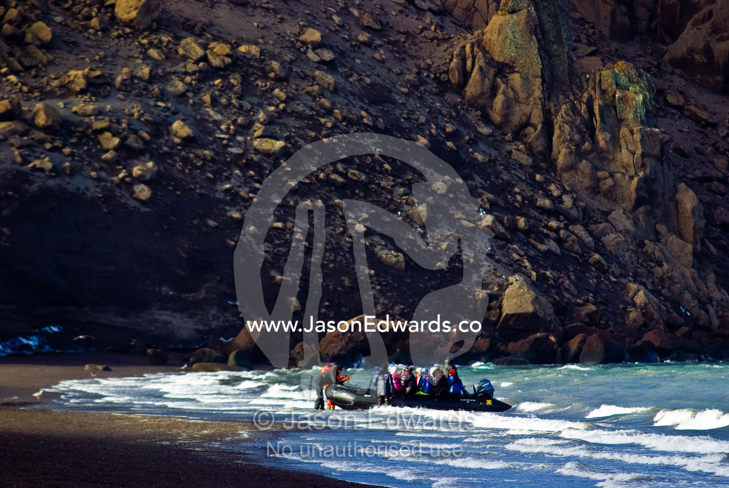 A zodiac boat deposits tourists ashore on a black volcanic beach. Whalers Bay, Antarctic Historic Site, Port Foster, Deception Island, South Shetland Islands, Antarctic Peninsula, Antarctica.