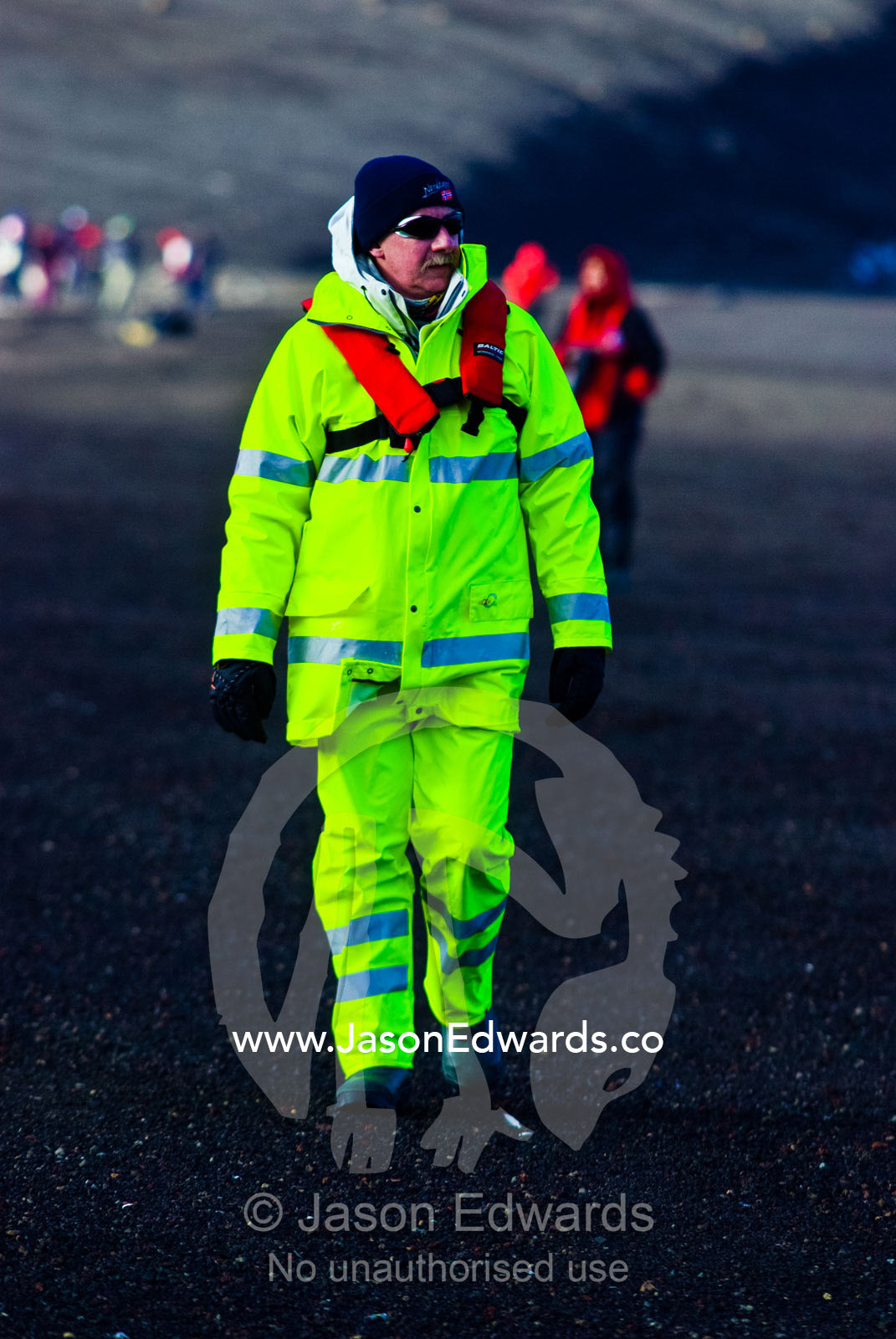 A tourist in fluorescent alpine clothing hiking on a volcanic beach. Whalers Bay, Antarctic Historic Site, Port Foster, Deception Island, South Shetland Islands, Antarctic Peninsula, Antarctica.