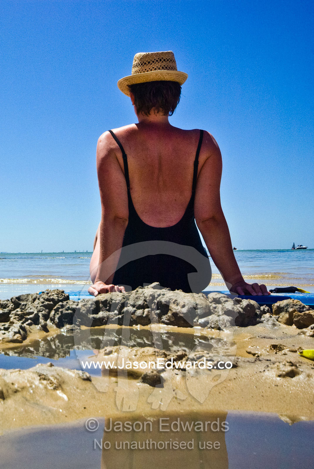 A woman in a straw hat and swim suit gets a sun tan on a summer beach. Rye Beach, Melbourne, Victoria, Australia.
