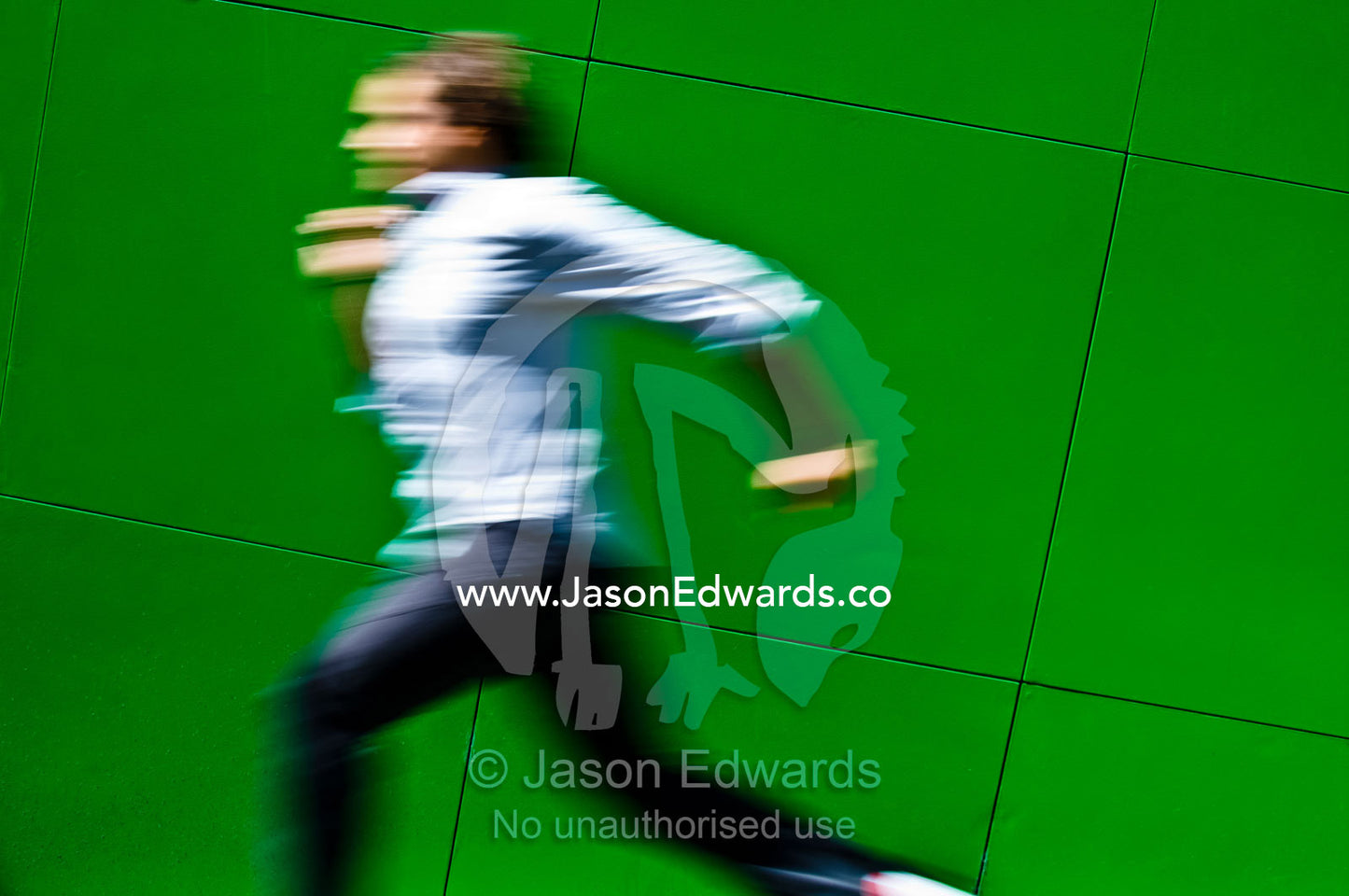 A man runs past a bright green architectural wall at high speed. Carlton, Melbourne, Victoria, Australia.
