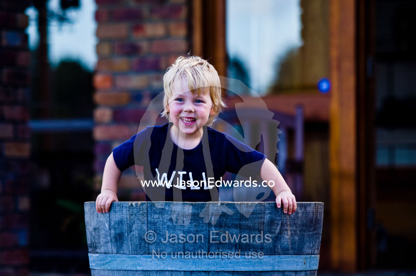 A young boy pops up from hiding in a wine barrel used as a pot plant. Witta, Sunshine Coast, Brisbane, Queensland, Australia.