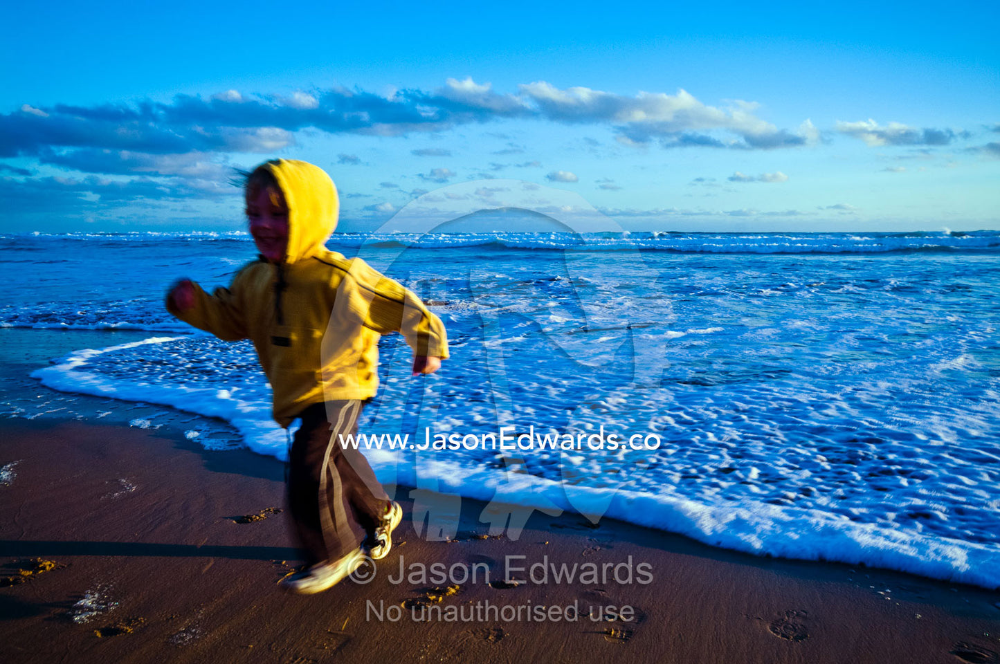 An excited young boy runs from approaching waves on a beach at sunset. Venus Bay, Bass Strait, South Gippsland, Victoria, Australia.