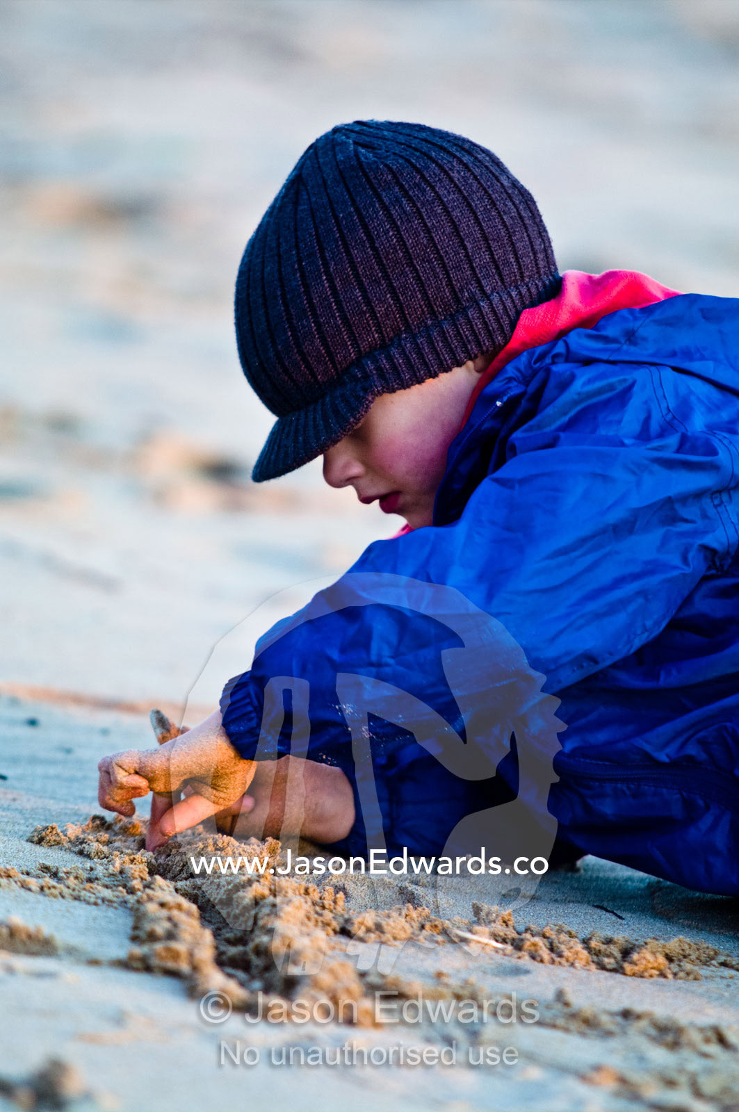 A boy rugged up on a windy beach concentrating on his sand games. Venus Bay, Bass Strait, South Gippsland, Victoria, Australia.