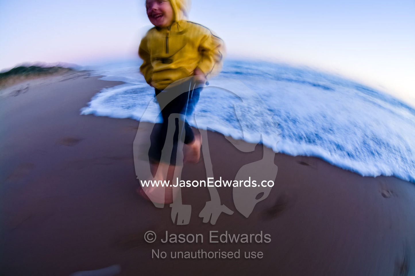 An excited young boy runs from approaching waves on a beach at sunset. Venus Bay, Bass Strait, South Gippsland, Victoria, Australia.