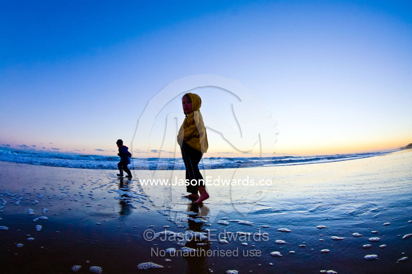 Two young friends play and explore on a beach at low tide at twilight. Venus Bay, Bass Strait, South Gippsland, Victoria, Australia.