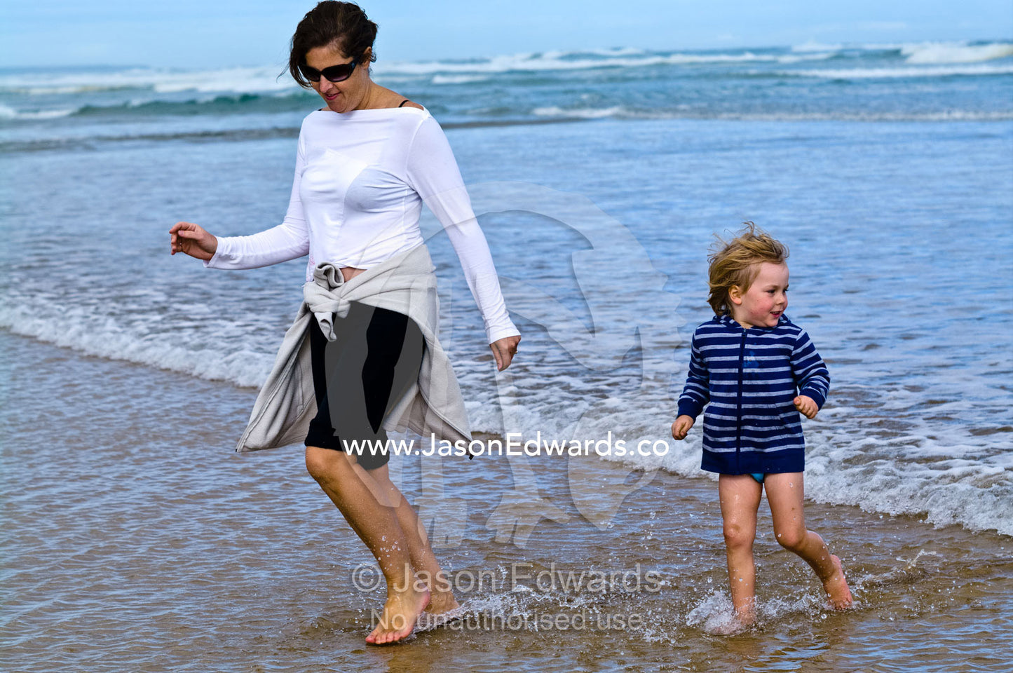 A mother and son run from approaching waves on a beach. Venus Bay, Bass Strait, South Gippsland, Victoria, Australia.