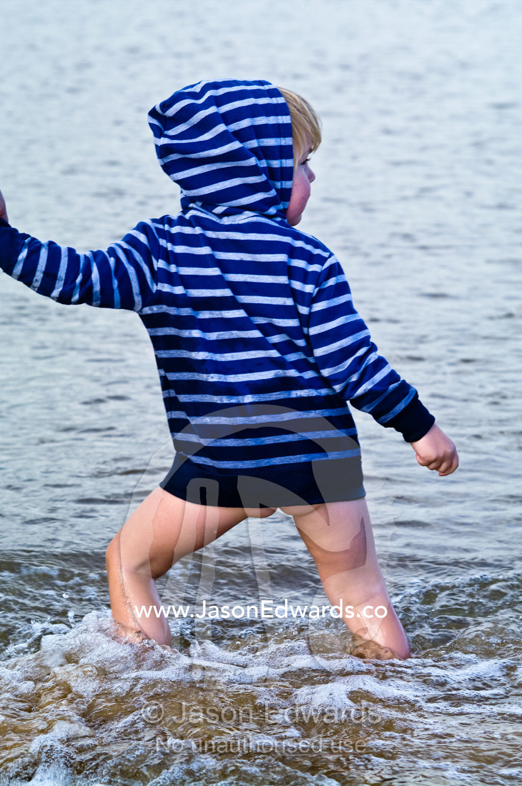 An excited and happy boy walks in the waves holding his mum's hand. Venus Bay, Bass Strait, South Gippsland, Victoria, Australia.