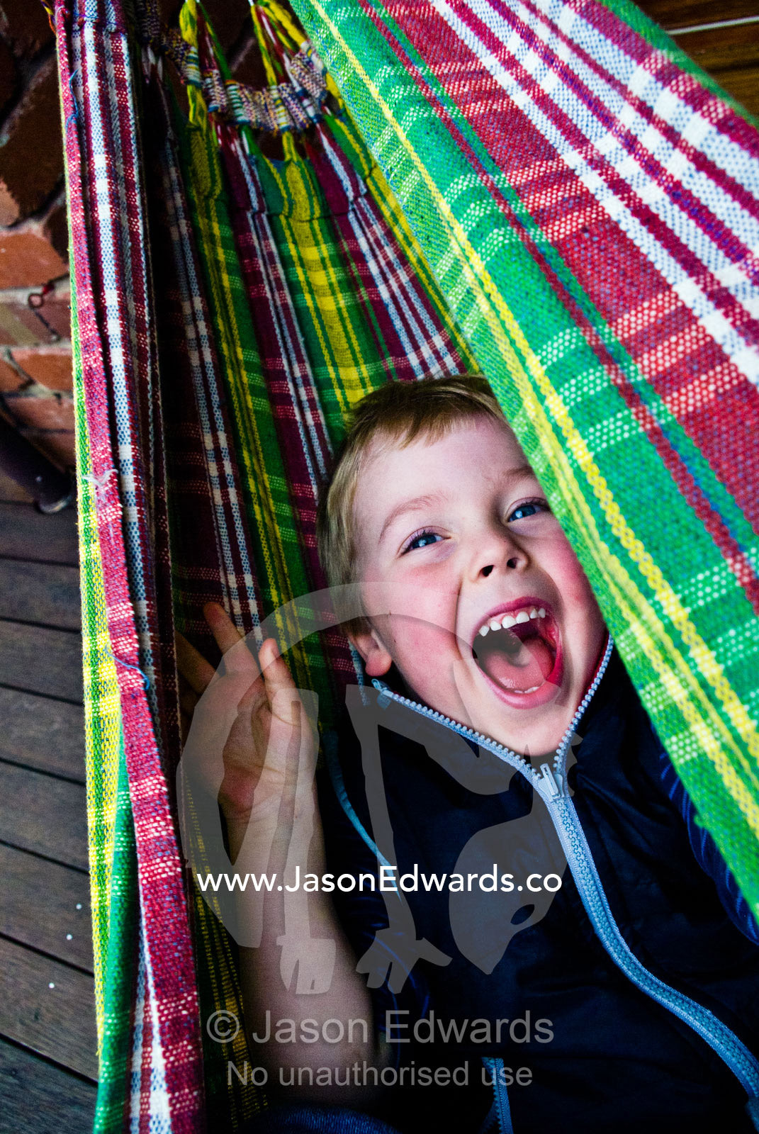 A young boy laughing hysterically whilst swinging in a tartan hammock. Carlton North, Melbourne, Victoria, Australia.