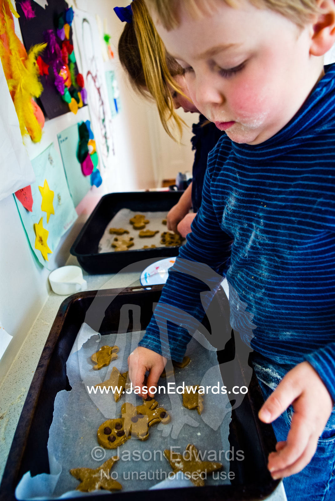 A young boy attaches eyes and buttons to his gingerbread men to bake. Carlton North, Melbourne, Victoria, Australia.