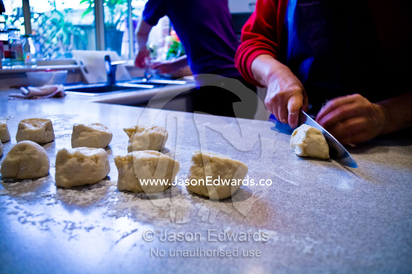 Chinese woman cuts traditional pork buns, baize, on a kitchen bench. Campsie, Syndey, New South Wales, Australia.