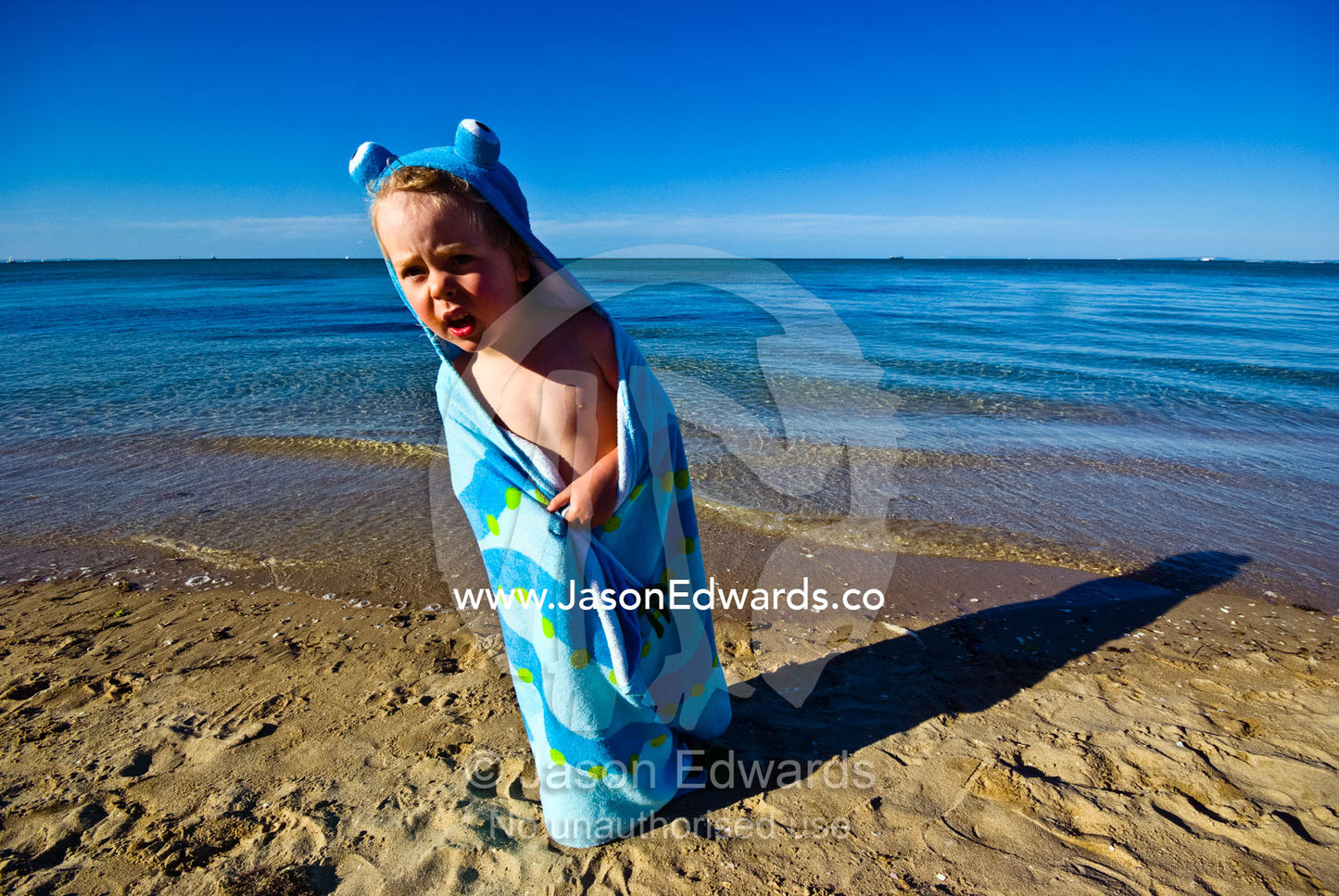 A boy on a beach keeps warm wrapped in an octopus towel after a swim. Rye Beach, Melbourne, Victoria, Australia.