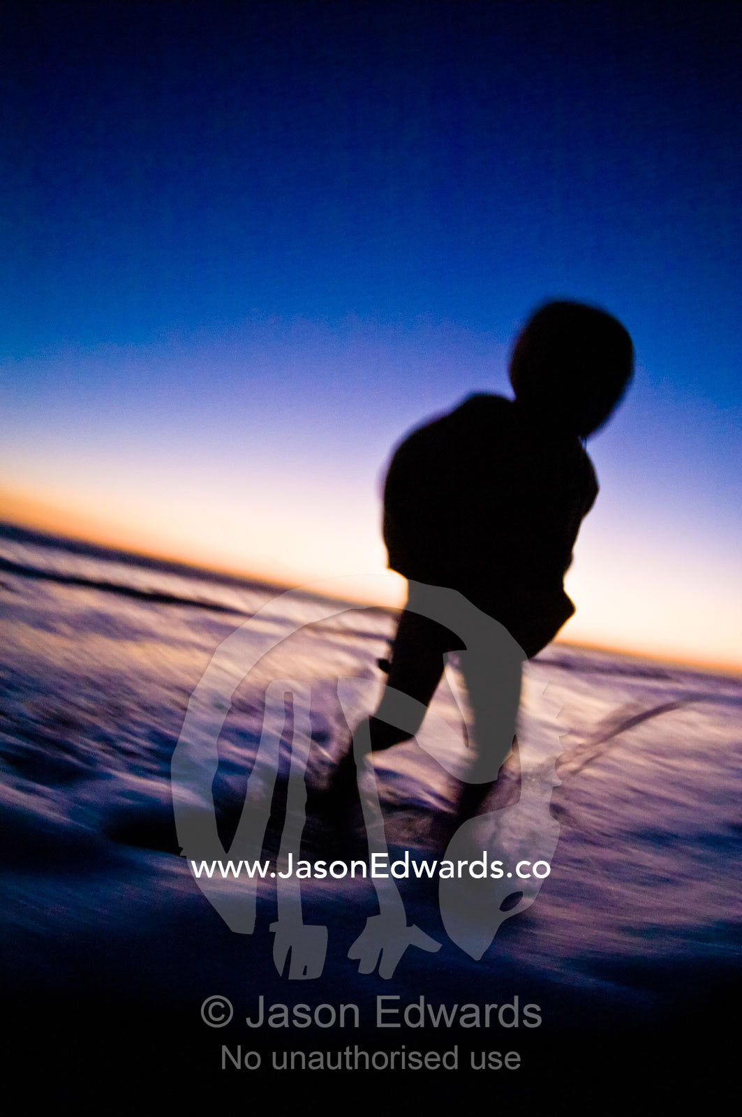 A small boy runs from waves on a remote stretch of beach at twilight. Venus Bay, Cape Liptrap Coastal Park, Bass Strait, South Gippsland, Victoria, Australia.