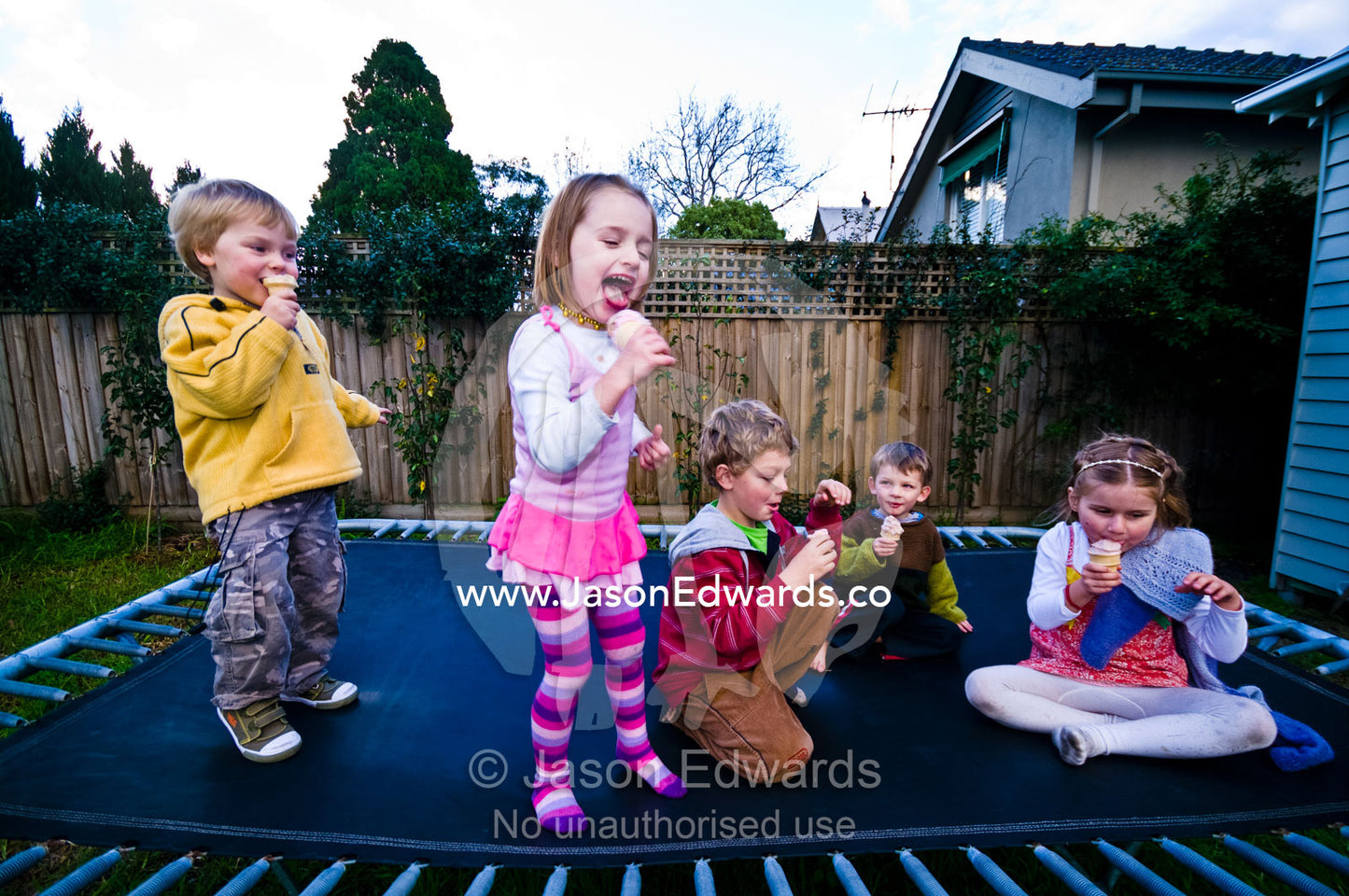 Cousins and friends playing on a trampoline whilst eating ice-cream. Malvern East, Melbourne, Victoria, Australia.