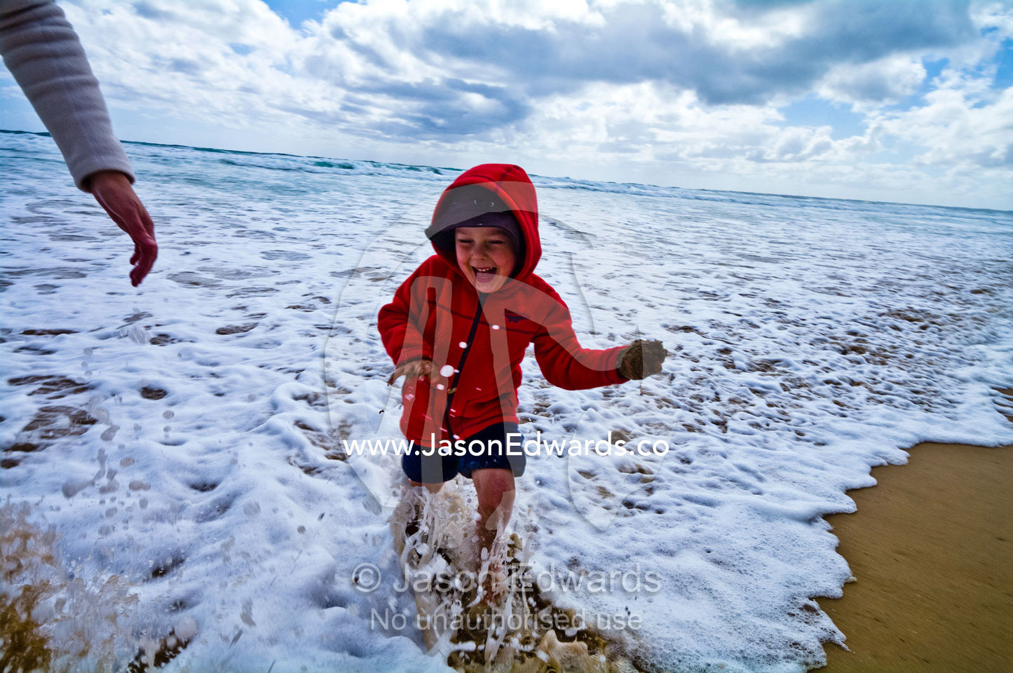 A young boy laughing and running in the foamy waves at the beach. Venus Bay, Cape Liptrap Coastal Park, Bass Strait, South Gippsland, Victoria, Australia.
