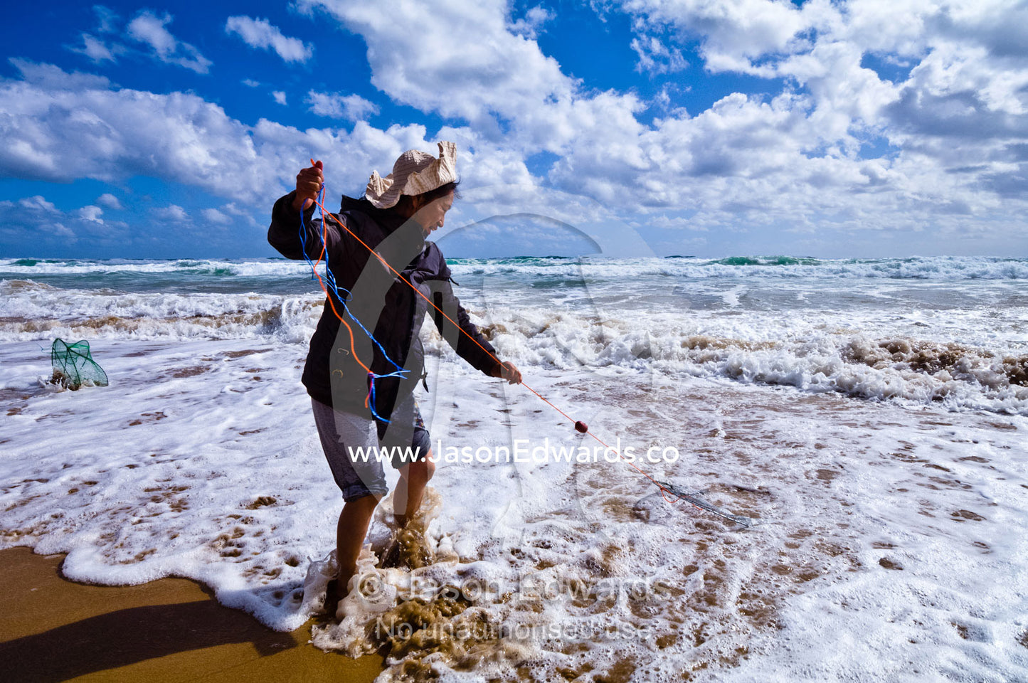 A woman fishes for pipi using a fishing line and basket in the surf. Venus Bay, Cape Liptrap Coastal Park, Bass Strait, South Gippsland, Victoria, Australia.